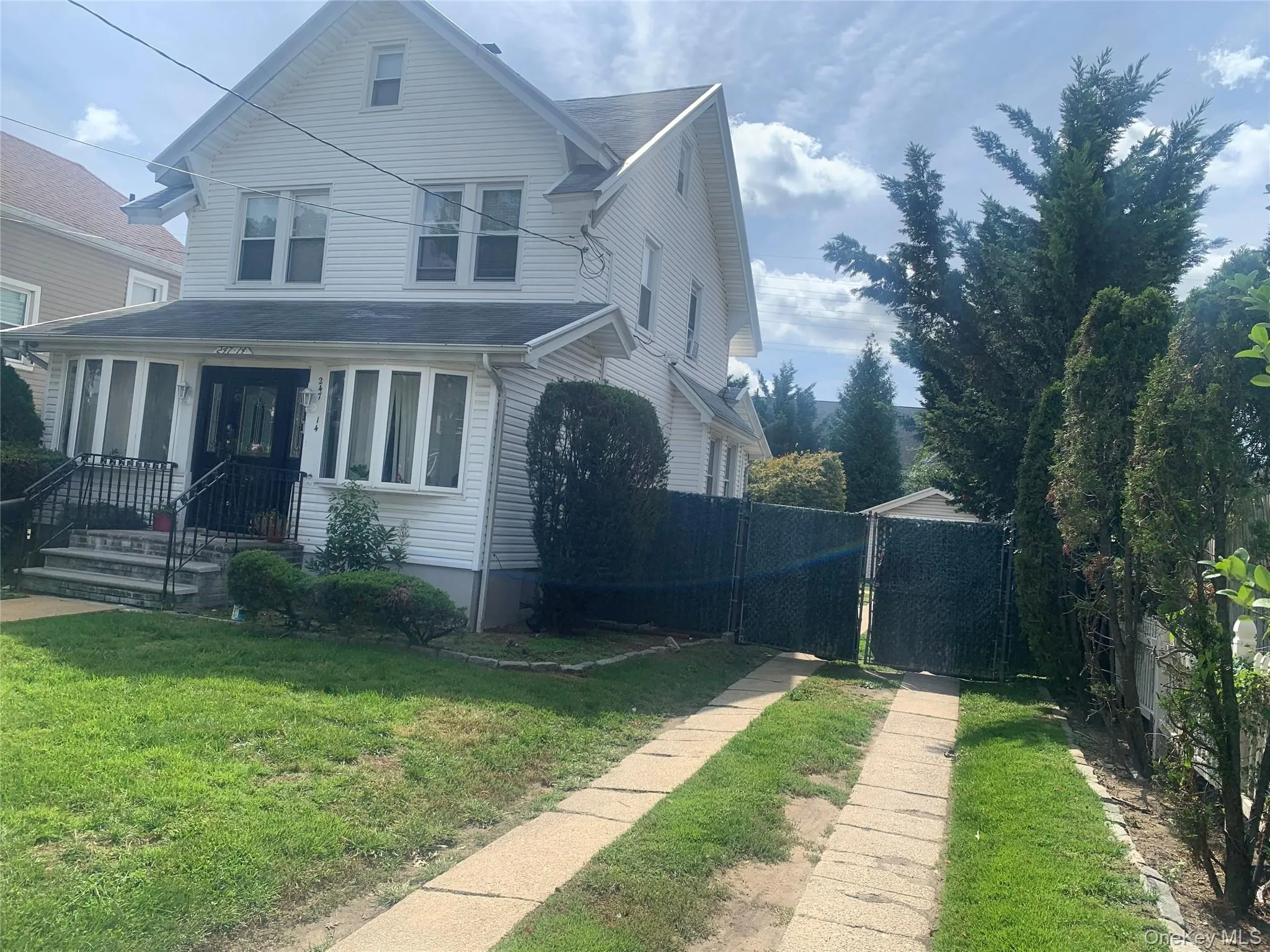 Two-story residence featuring a covered front porch, bay windows, a paved driveway, and an enclosed side yard with mature trees Two-story residence featuring a covered front porch, bay windows, a paved driveway, and an enclosed side yard with mature trees