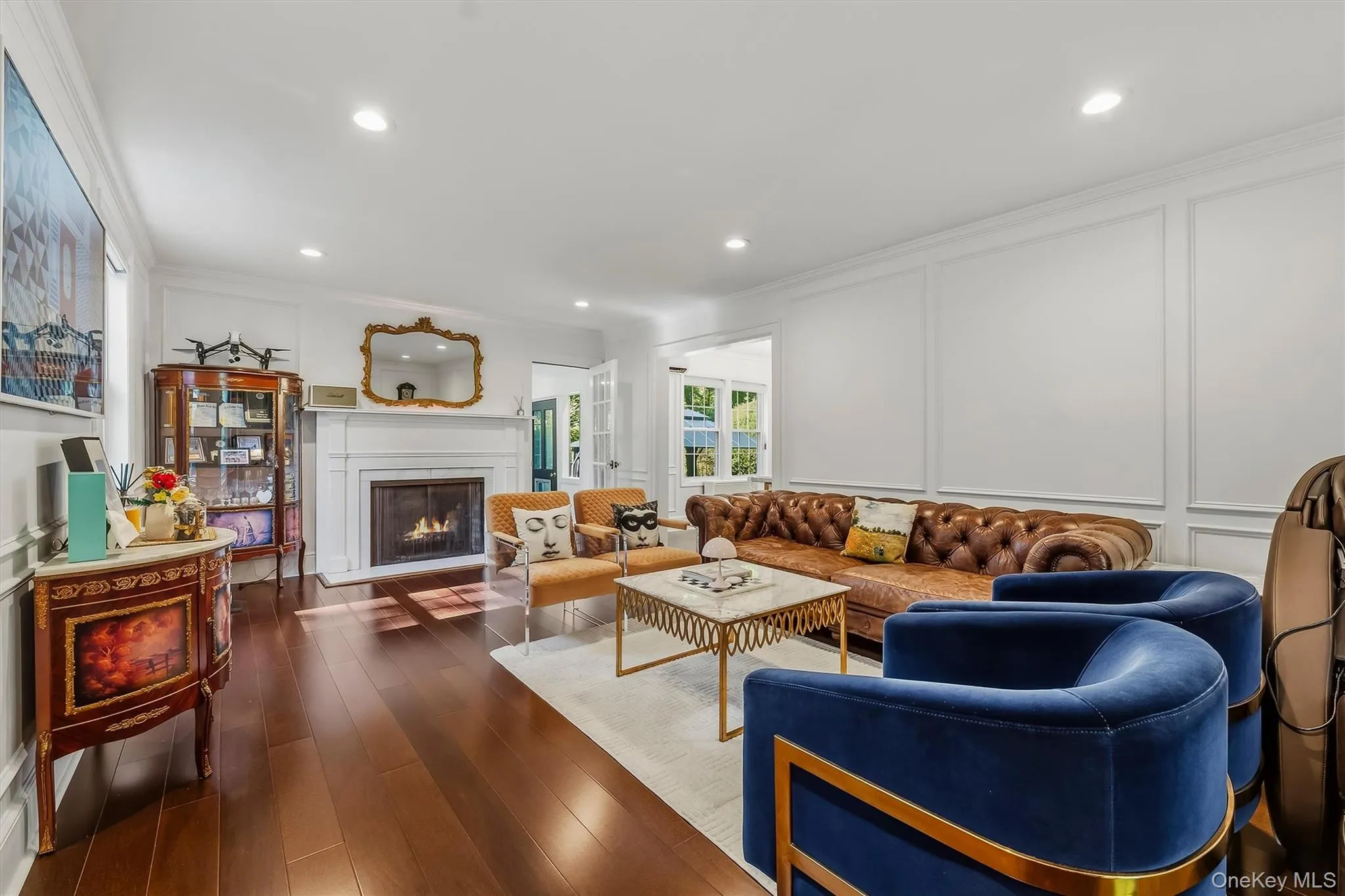 Hardwood-finish flooring, white paneled walls, recessed lighting, white fireplace with a mantel Hardwood-finish flooring, white paneled walls, recessed lighting, white fireplace with a mantel