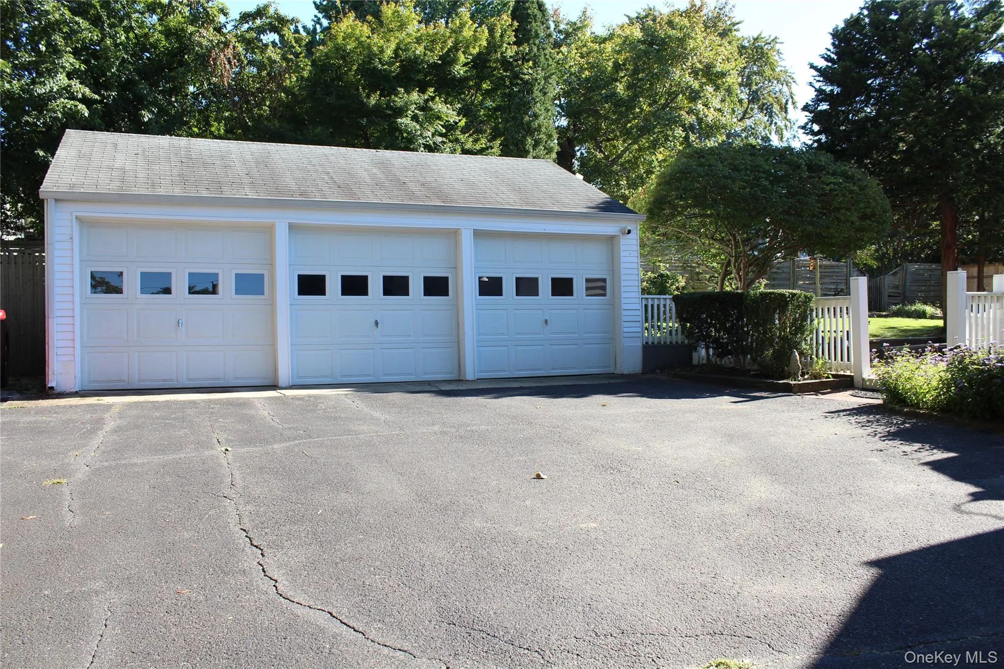 Three-car garage with white paneled doors, white exterior siding, and a gabled roof Three-car garage with white paneled doors, white exterior siding, and a gabled roof