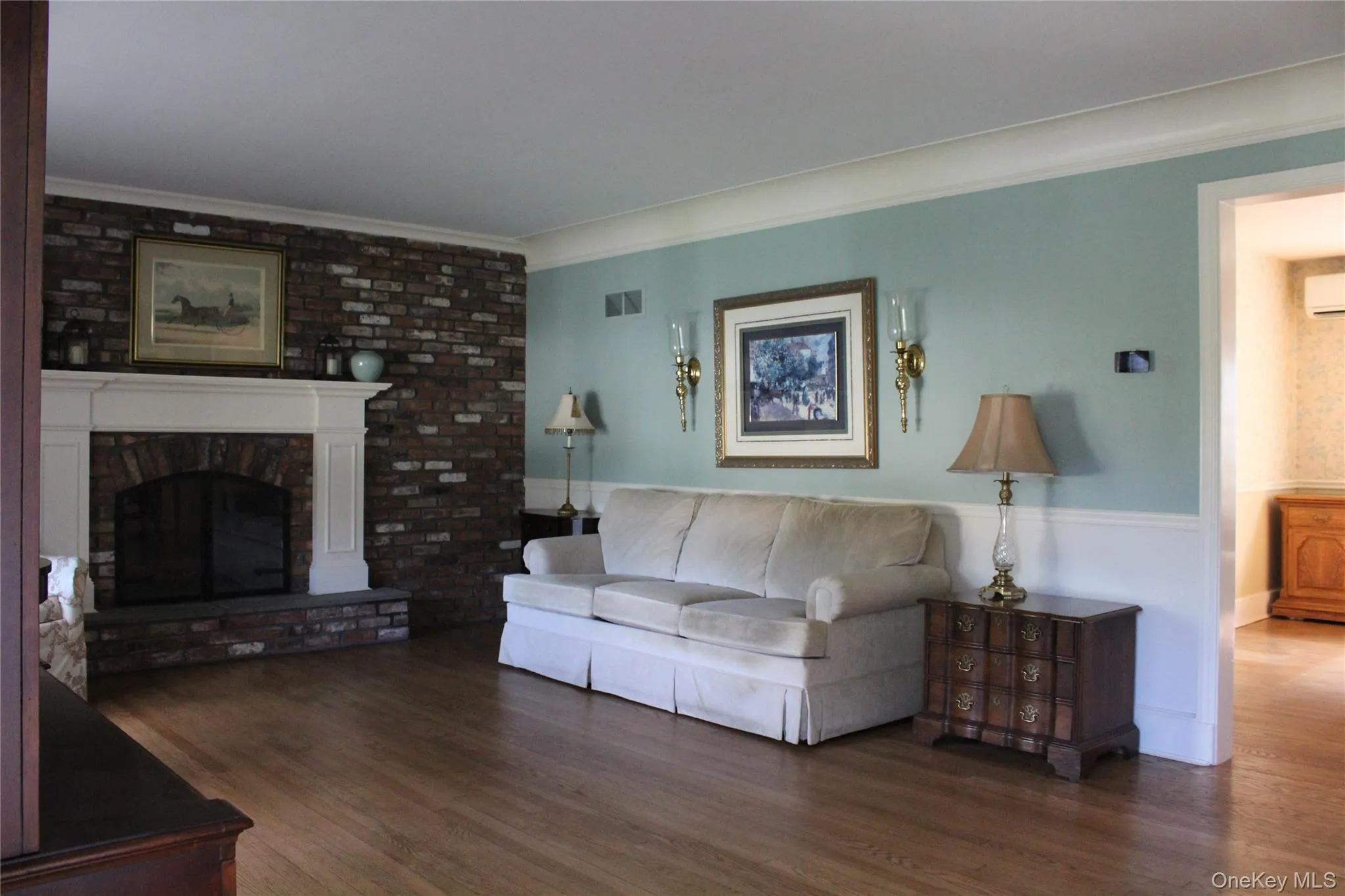 Hardwood flooring, brick-surround fireplace with white mantel, two-tone wall treatment, and wall sconces Hardwood flooring, brick-surround fireplace with white mantel, two-tone wall treatment, and wall sconces