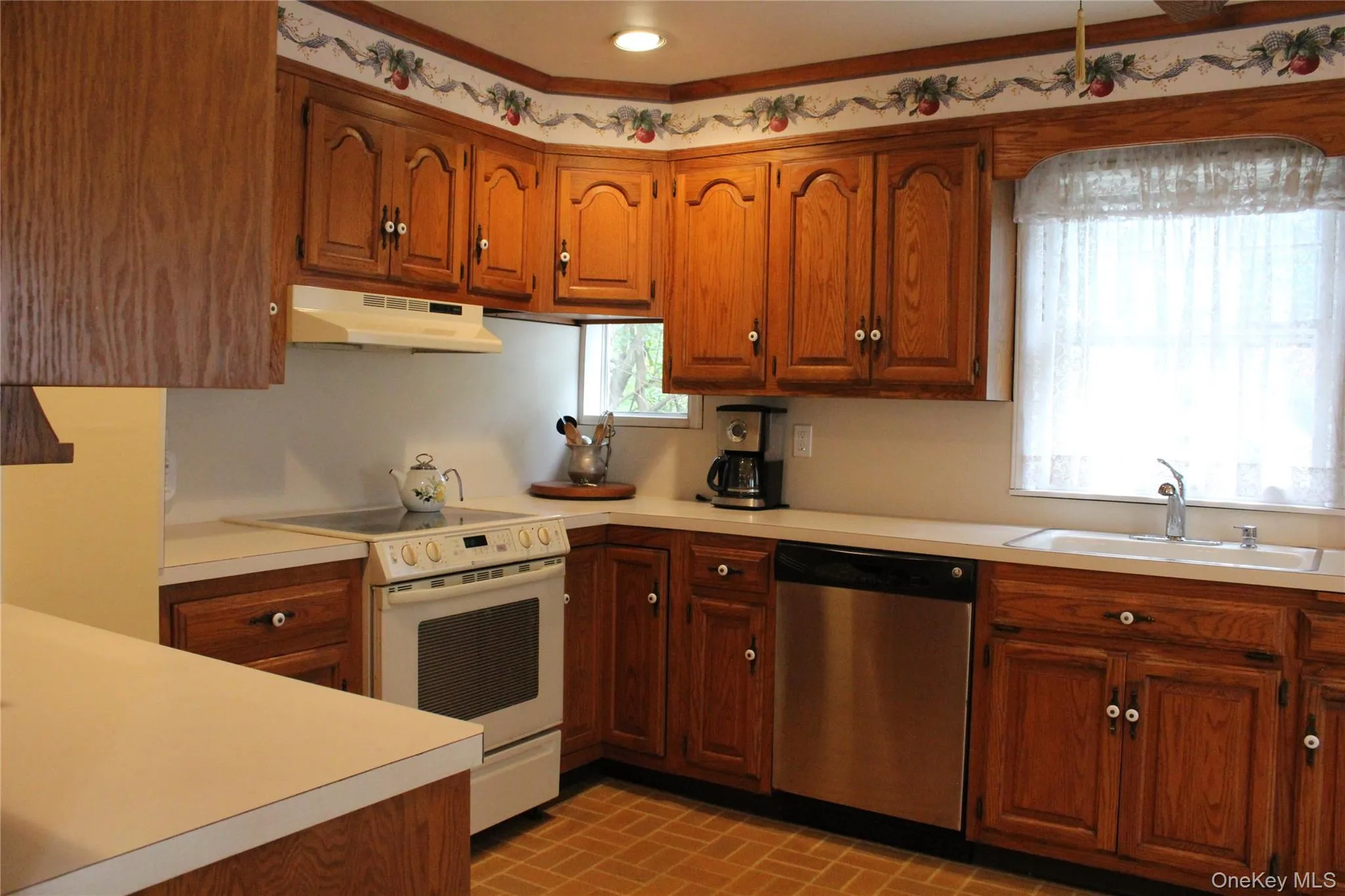 Wood-finish cabinetry, white countertops, built-in SS dishwasher, and range with overhead vent Wood-finish cabinetry, white countertops, built-in SS dishwasher, and range with overhead vent