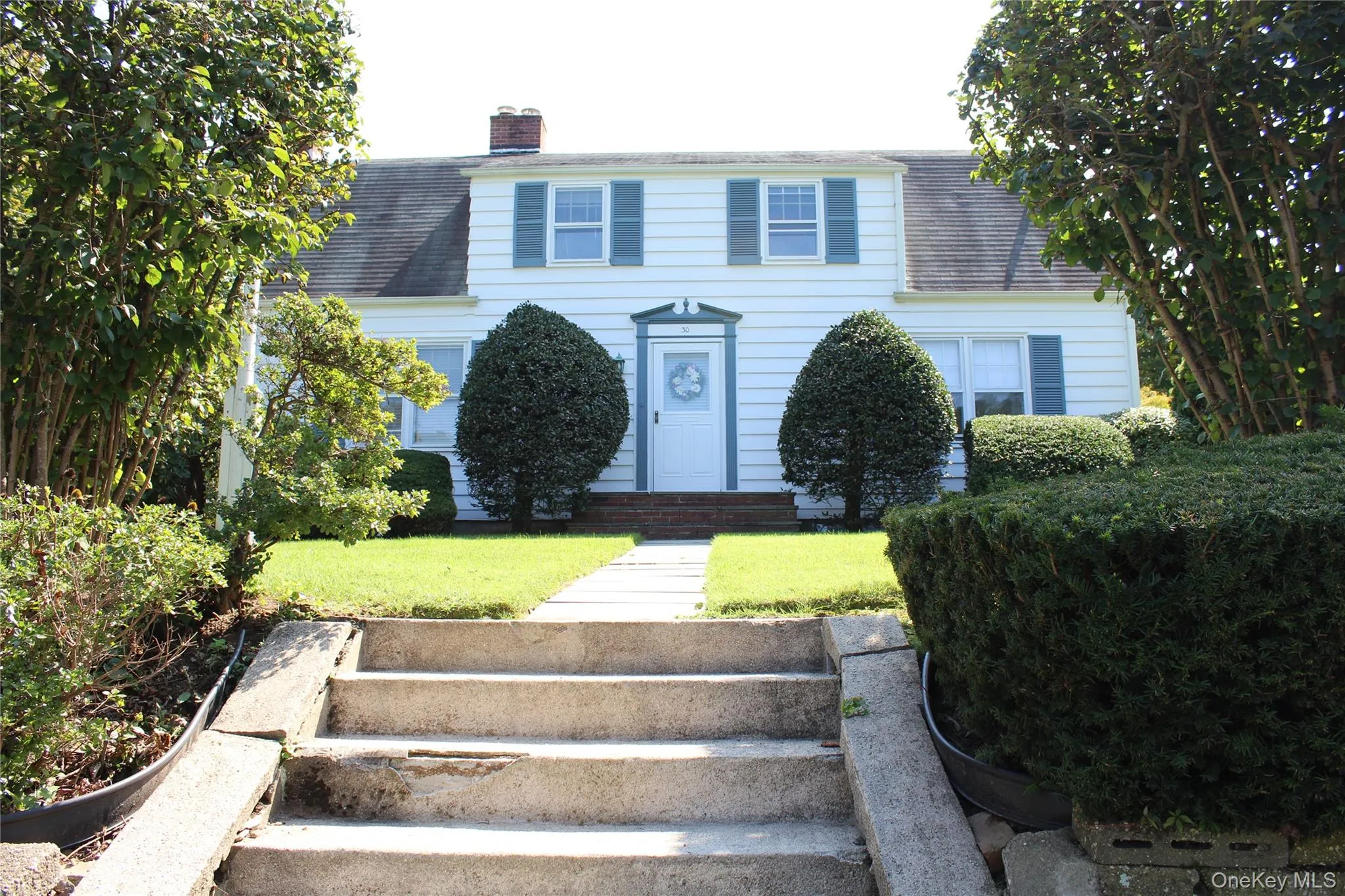 White siding exterior with green window shutters, a front entry door with a decorative wreath, and concrete steps leading to a additional grass then street White siding exterior with green window shutters, a front entry door with a decorative wreath, and concrete steps leading to a additional grass then street