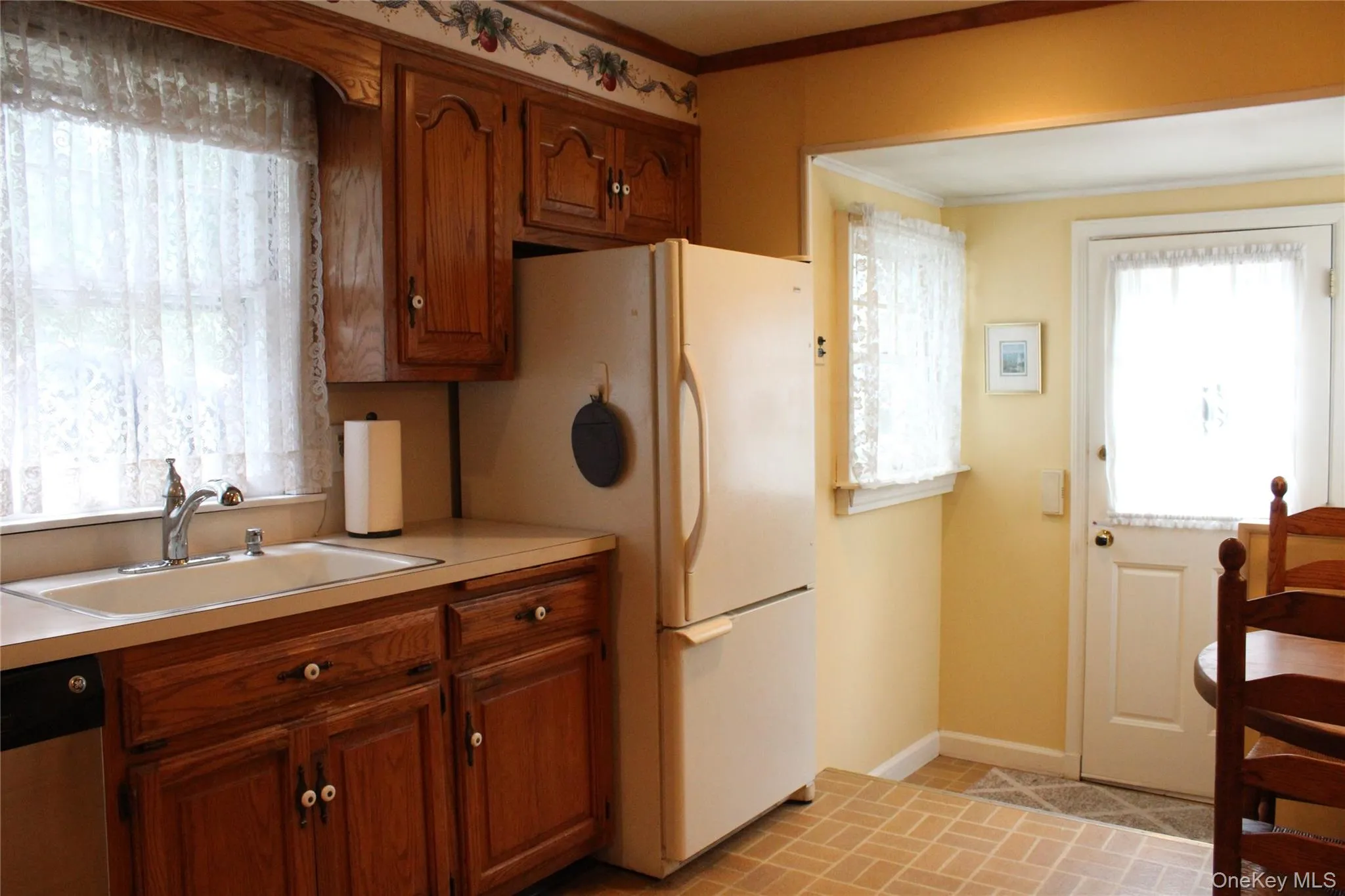 Wood cabinetry, white sink basin, Refrig and light-toned countertops. Wood cabinetry, white sink basin, Refrig and light-toned countertops.