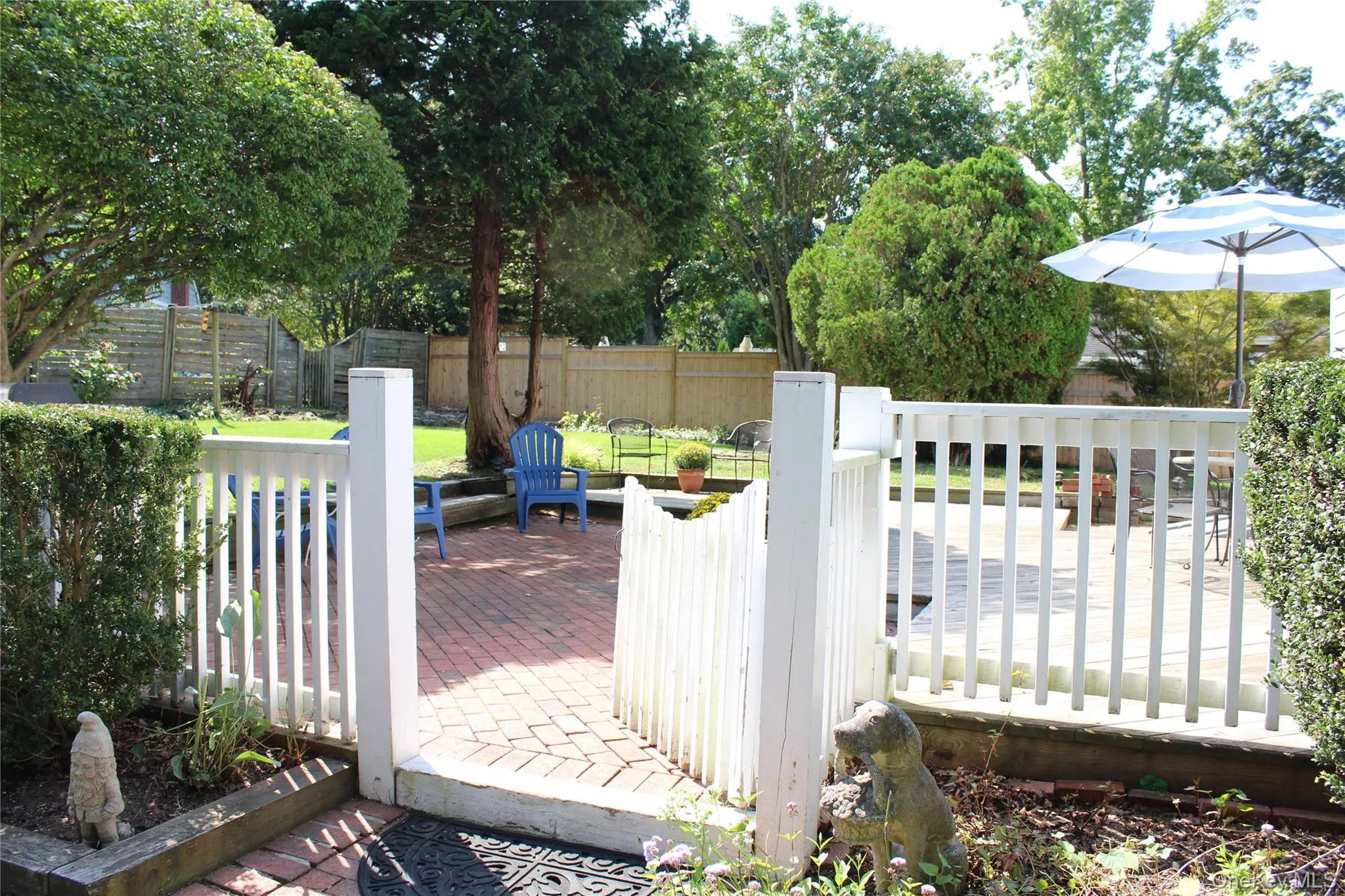 Brick paver patio, Deck area with white picket fence, surrounded by established lawn, landscaping and mature trees Brick paver patio, Deck area with white picket fence, surrounded by established lawn, landscaping and mature trees