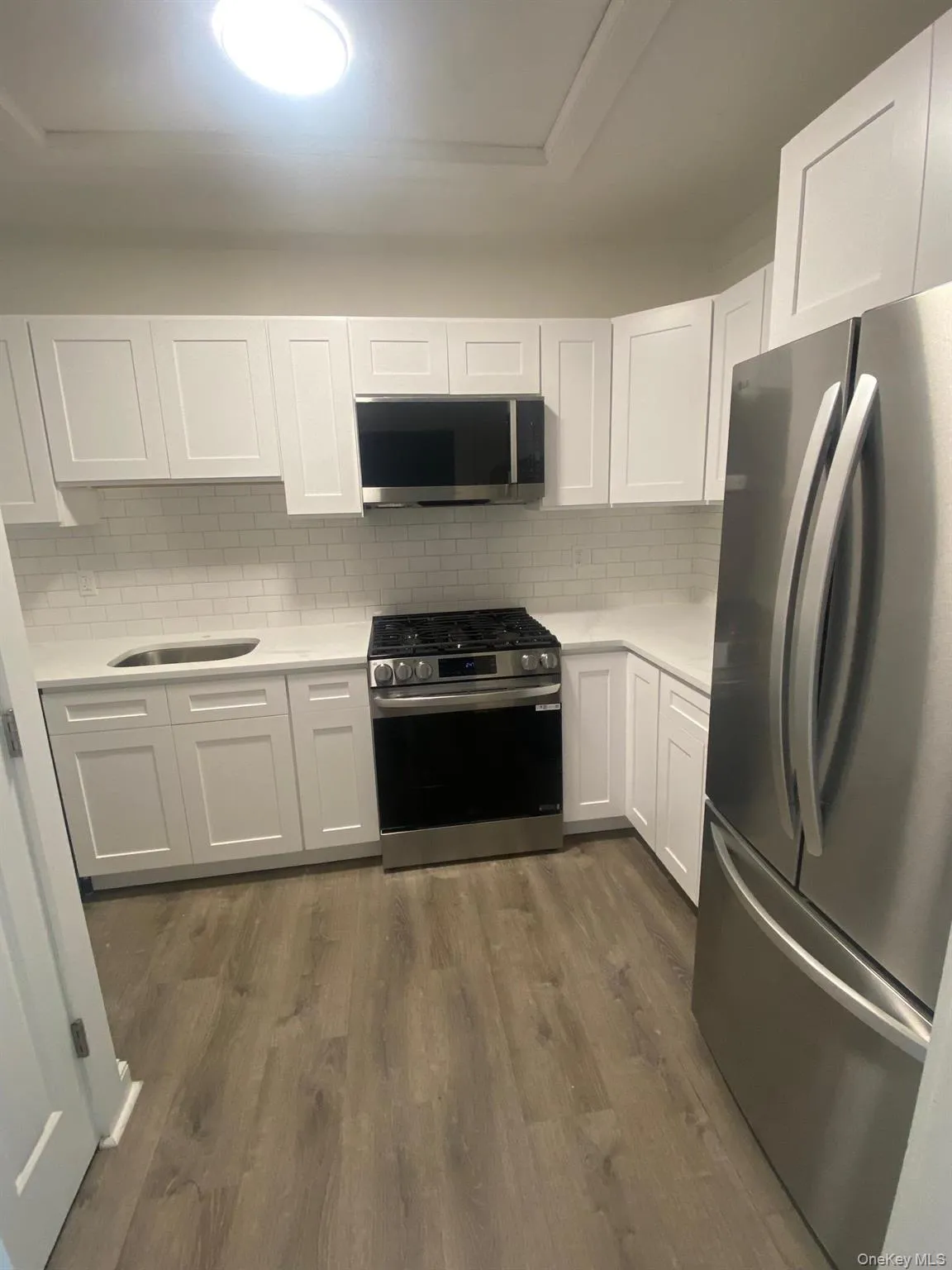 Kitchen featuring stainless steel appliances, light countertops, white cabinetry, dark wood-type flooring, and tasteful backsplash Kitchen featuring stainless steel appliances, light countertops, white cabinetry, dark wood-type flooring, and tasteful backsplash