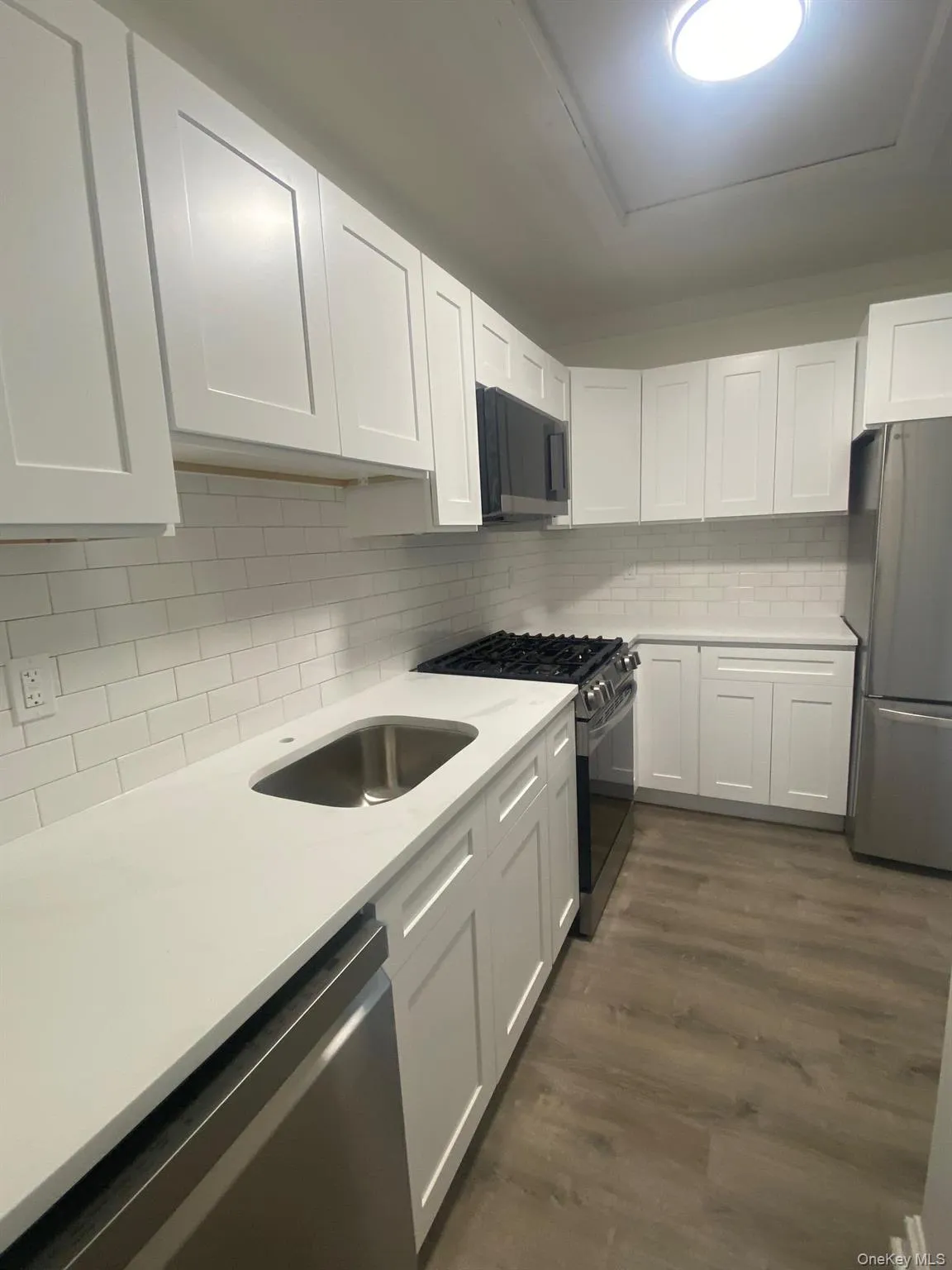 Kitchen with black appliances, light countertops, white cabinets, decorative backsplash, and dark wood-style flooring Kitchen with black appliances, light countertops, white cabinets, decorative backsplash, and dark wood-style flooring