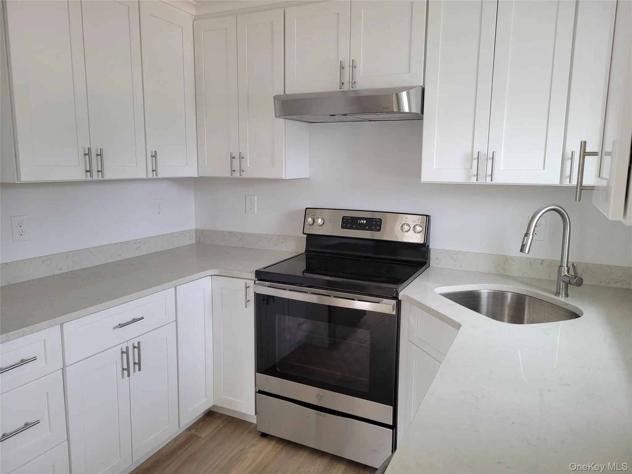 Kitchen with electric range, under cabinet range hood, white cabinetry, and light wood-type flooring Kitchen with electric range, under cabinet range hood, white cabinetry, and light wood-type flooring