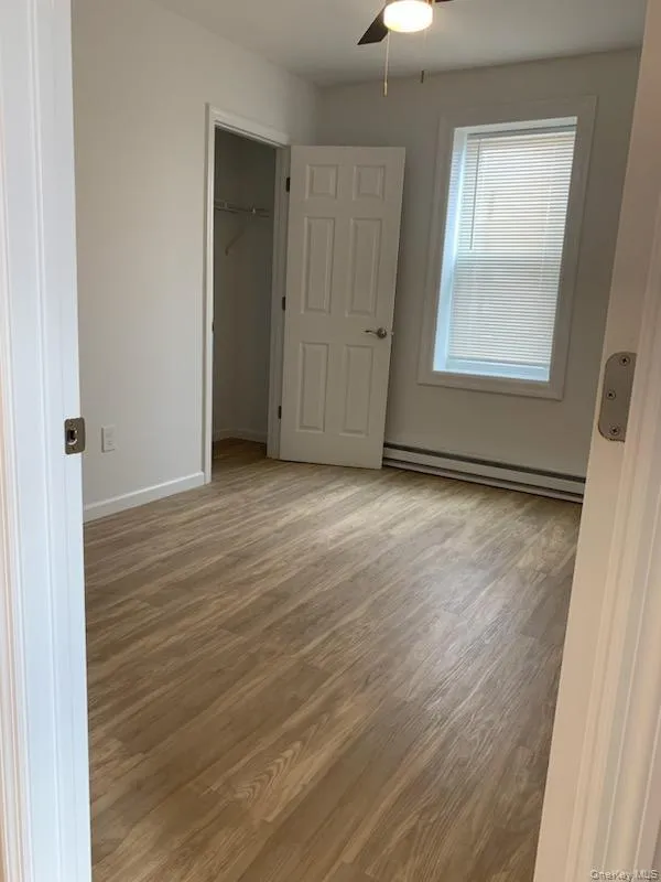 Unfurnished bedroom featuring baseboard heating, wood finished floors, a closet, and a ceiling fan Unfurnished bedroom featuring baseboard heating, wood finished floors, a closet, and a ceiling fan