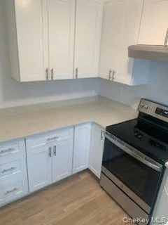 Kitchen featuring stainless steel electric stove, light countertops, exhaust hood, light wood-style floors, and white cabinetry Kitchen featuring stainless steel electric stove, light countertops, exhaust hood, light wood-style floors, and white cabinetry
