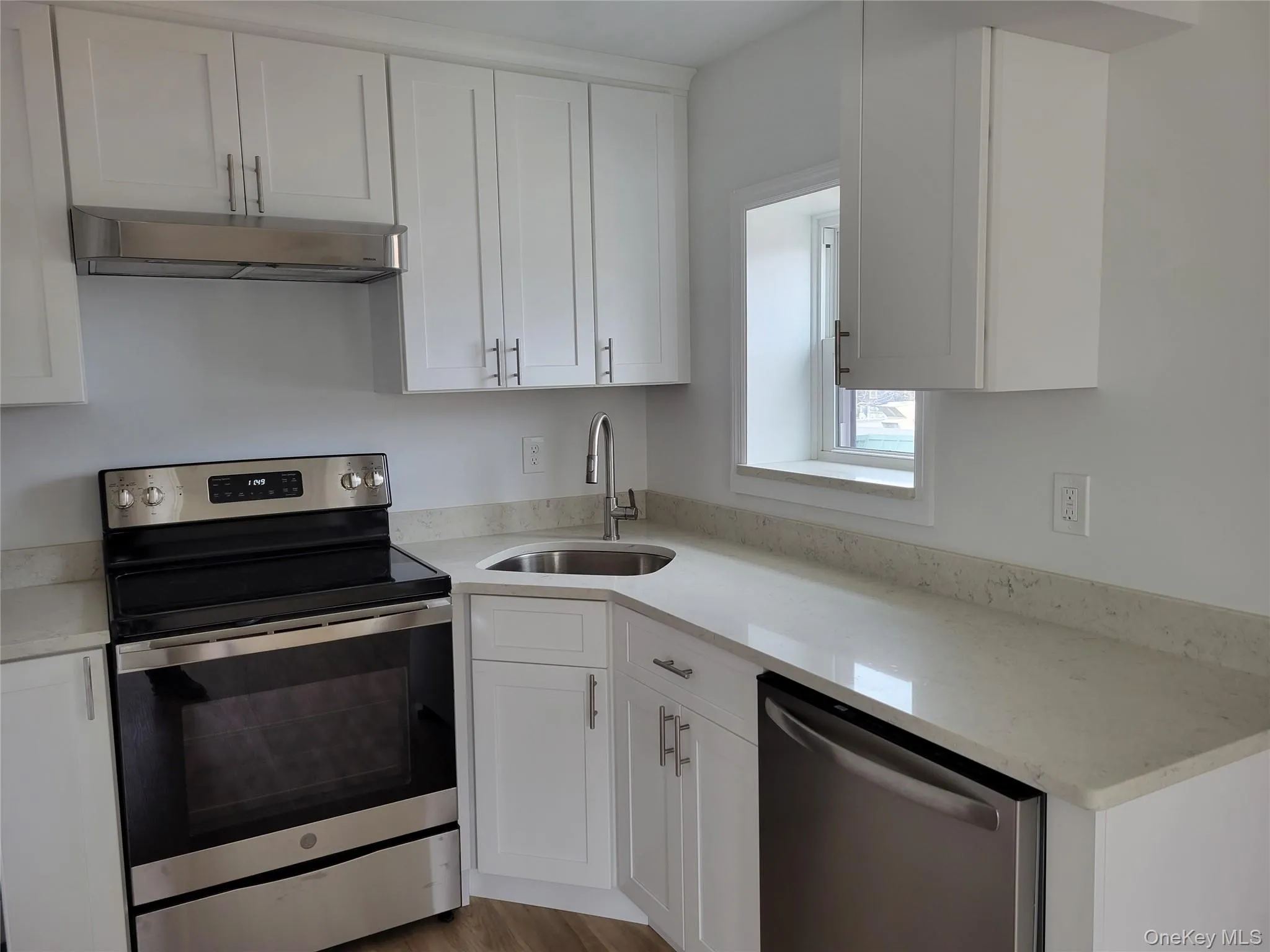 Kitchen with appliances with stainless steel finishes, range hood, white cabinets, and light stone countertops Kitchen with appliances with stainless steel finishes, range hood, white cabinets, and light stone countertops