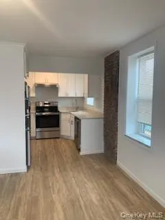 Kitchen featuring electric range, light wood-type flooring, white cabinets, dishwashing machine, and range hood Kitchen featuring electric range, light wood-type flooring, white cabinets, dishwashing machine, and range hood