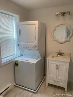 Laundry room featuring stacked washer / drying machine, light wood-type flooring, and a baseboard heating unit Laundry room featuring stacked washer / drying machine, light wood-type flooring, and a baseboard heating unit