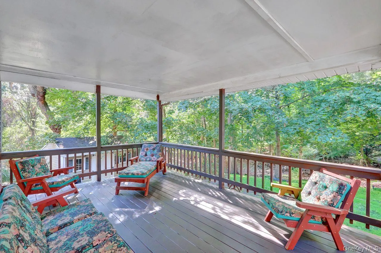 Covered outdoor deck with wood flooring and dark wood railings, surrounded by mature trees Covered outdoor deck with wood flooring and dark wood railings, surrounded by mature trees