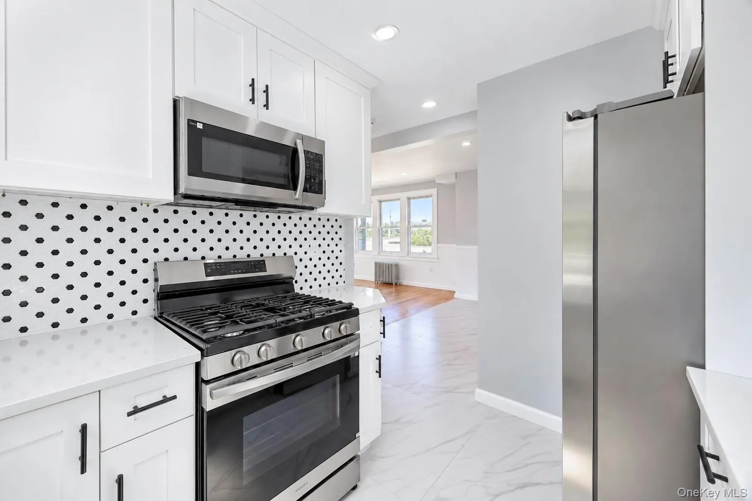 Kitchen featuring white cabinetry, stainless steel appliances, a unique polka-dot backsplash, and white countertops Kitchen featuring white cabinetry, stainless steel appliances, a unique polka-dot backsplash, and white countertops