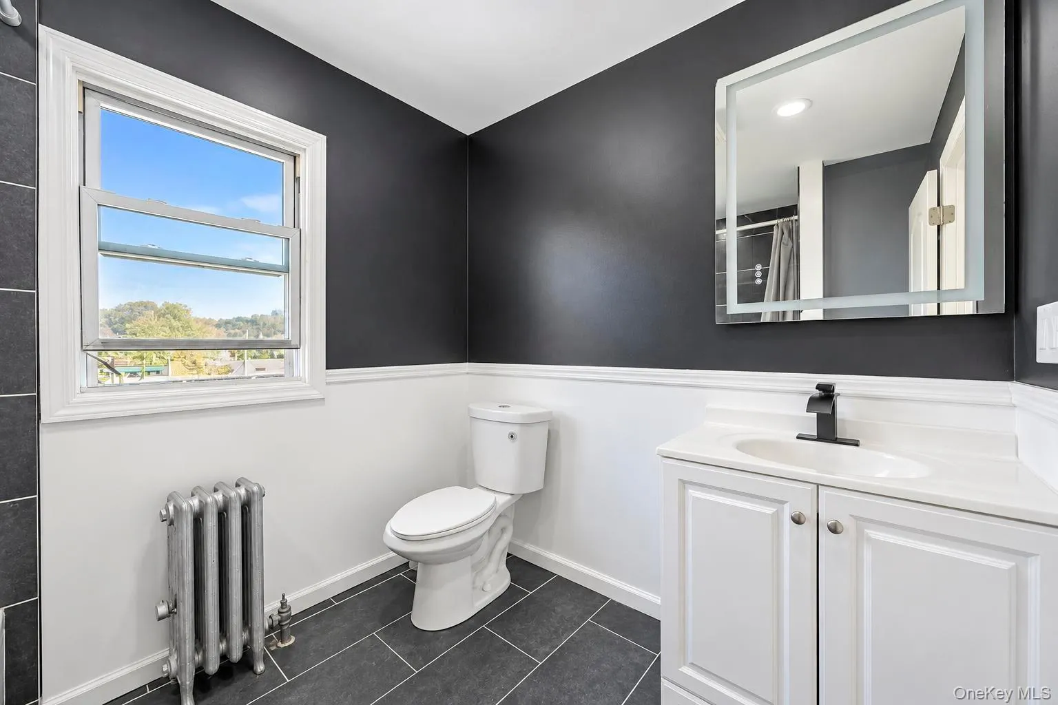 Modern bathroom with white wainscoting, dark wall color, white window frame, vanity with white cabinetry, and matte black faucet Modern bathroom with white wainscoting, dark wall color, white window frame, vanity with white cabinetry, and matte black faucet