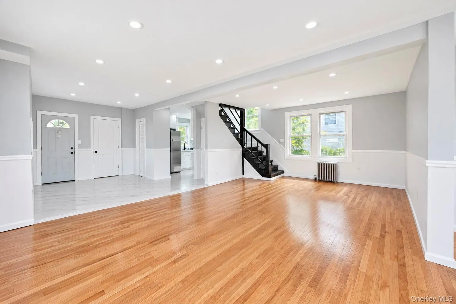 Hardwood flooring, recessed lighting, wainscoting, white trim, and a dark wood staircase with wrought iron balusters Hardwood flooring, recessed lighting, wainscoting, white trim, and a dark wood staircase with wrought iron balusters