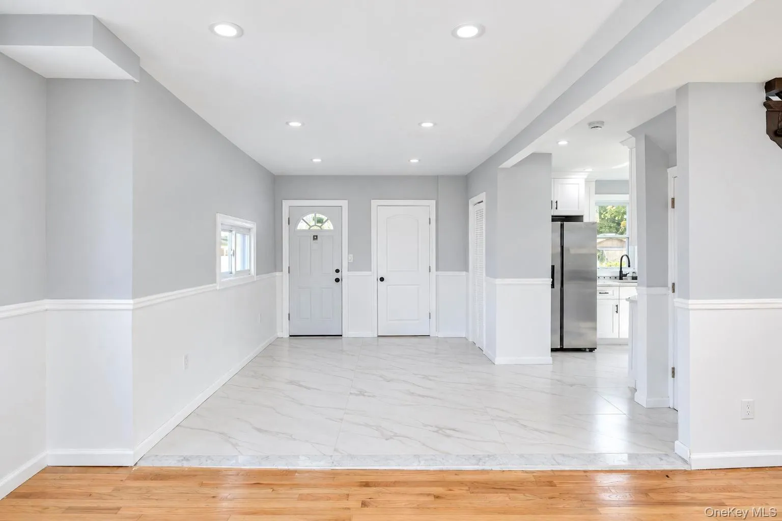 Recessed lighting, wood-finish flooring, half-wall wainscoting, stainless steel refrigerator, and white cabinetry Recessed lighting, wood-finish flooring, half-wall wainscoting, stainless steel refrigerator, and white cabinetry