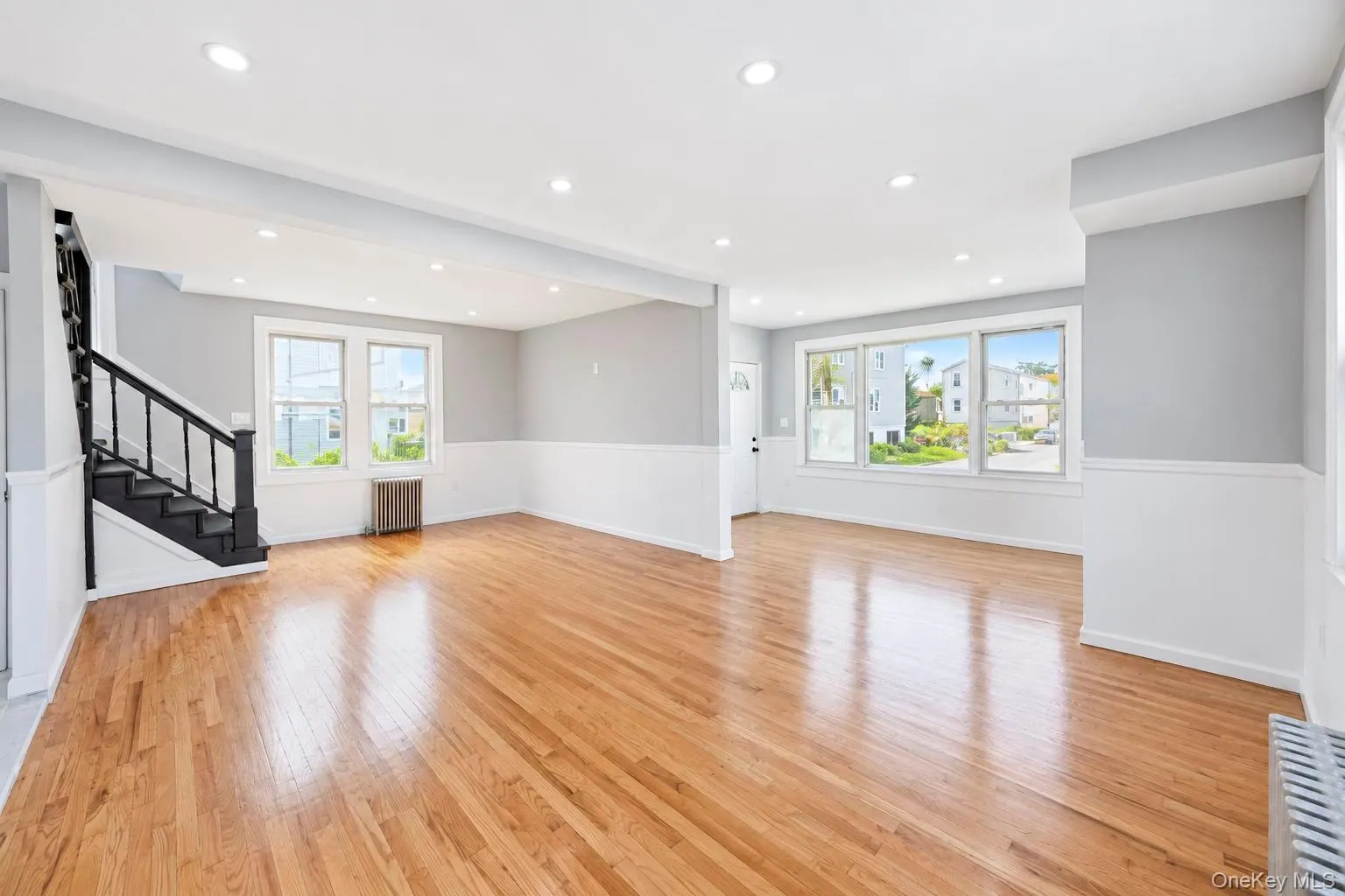 Hardwood flooring, recessed lighting, multiple windows, wainscoting, and a staircase with a black banister Hardwood flooring, recessed lighting, multiple windows, wainscoting, and a staircase with a black banister