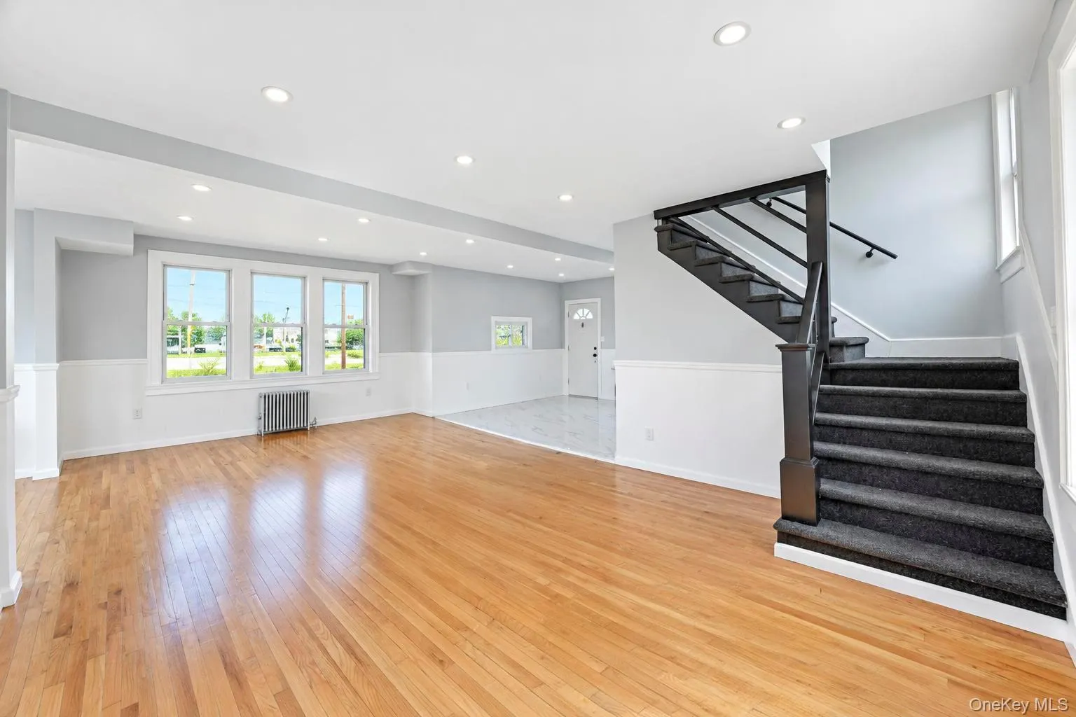 Hardwood flooring, recessed lighting, wainscoting, carpeted staircase with black railing, and multiple windows Hardwood flooring, recessed lighting, wainscoting, carpeted staircase with black railing, and multiple windows