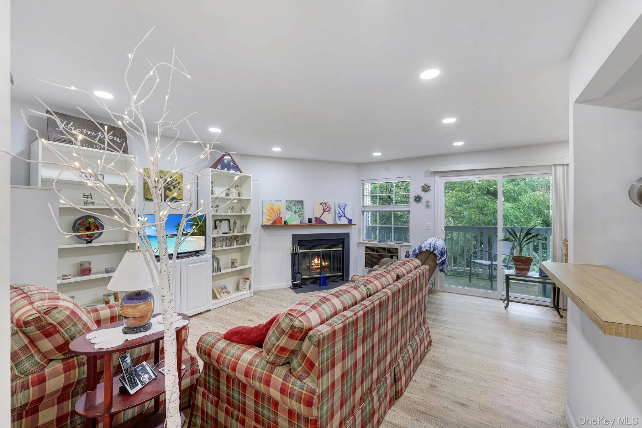 Recessed lighting, wood-finish flooring, built-in shelving, fireplace, and sliding glass door to exterior balcony Recessed lighting, wood-finish flooring, built-in shelving, fireplace, and sliding glass door to exterior balcony