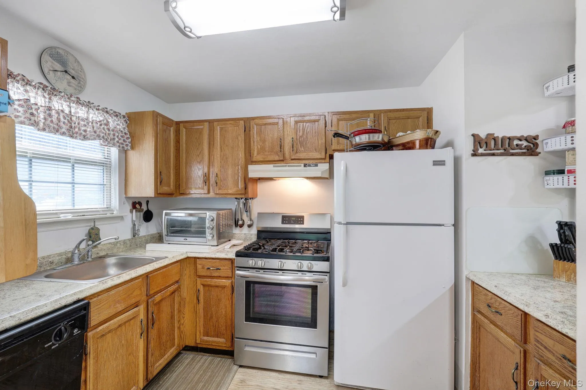 Kitchen featuring wood cabinetry, light-toned countertops, a stainless steel gas range, and a double-basin stainless steel sink Kitchen featuring wood cabinetry, light-toned countertops, a stainless steel gas range, and a double-basin stainless steel sink