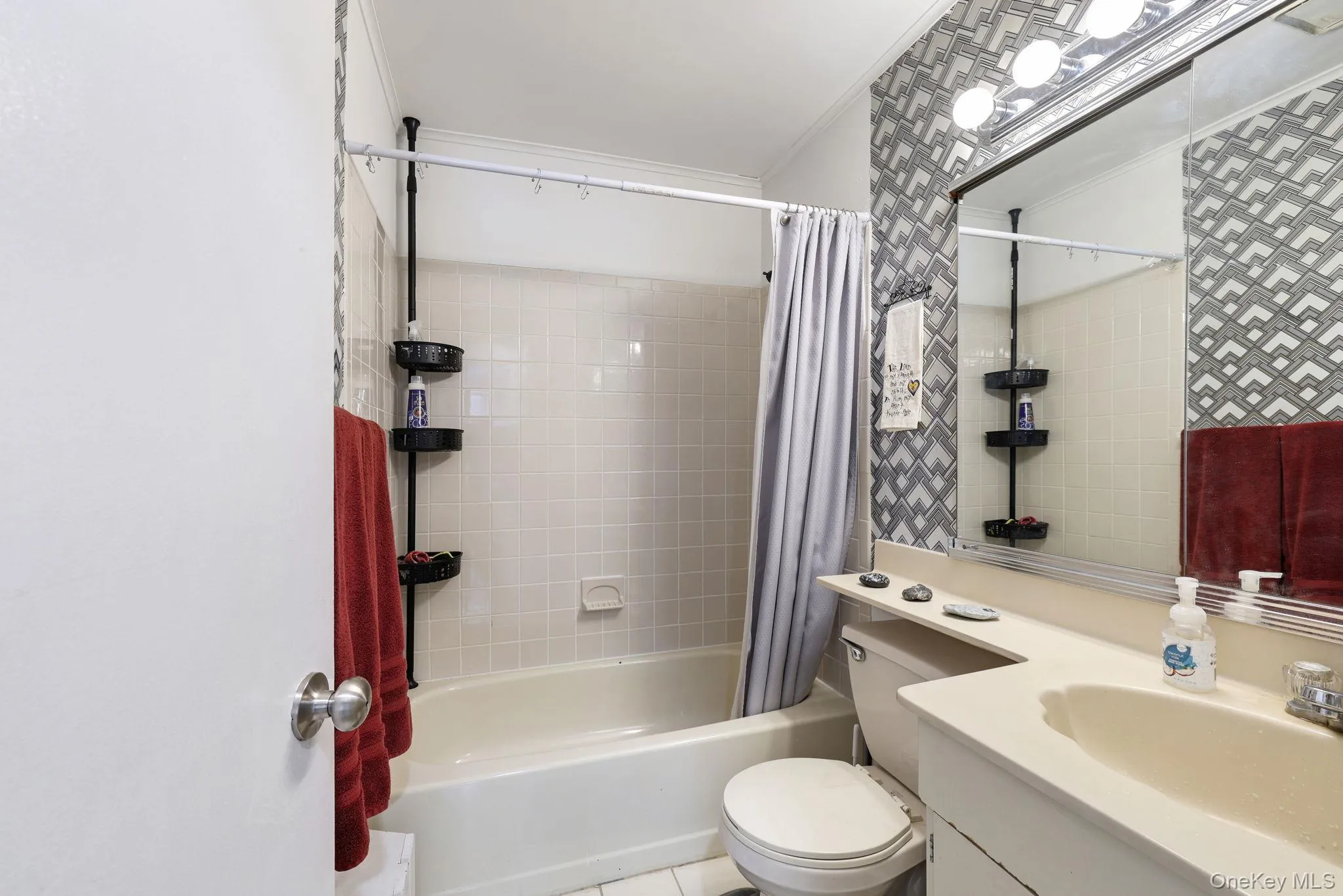 Bathroom featuring a full vanity with an integrated sink, a built-in bathtub with tiled surround, and decorative wall covering Bathroom featuring a full vanity with an integrated sink, a built-in bathtub with tiled surround, and decorative wall covering