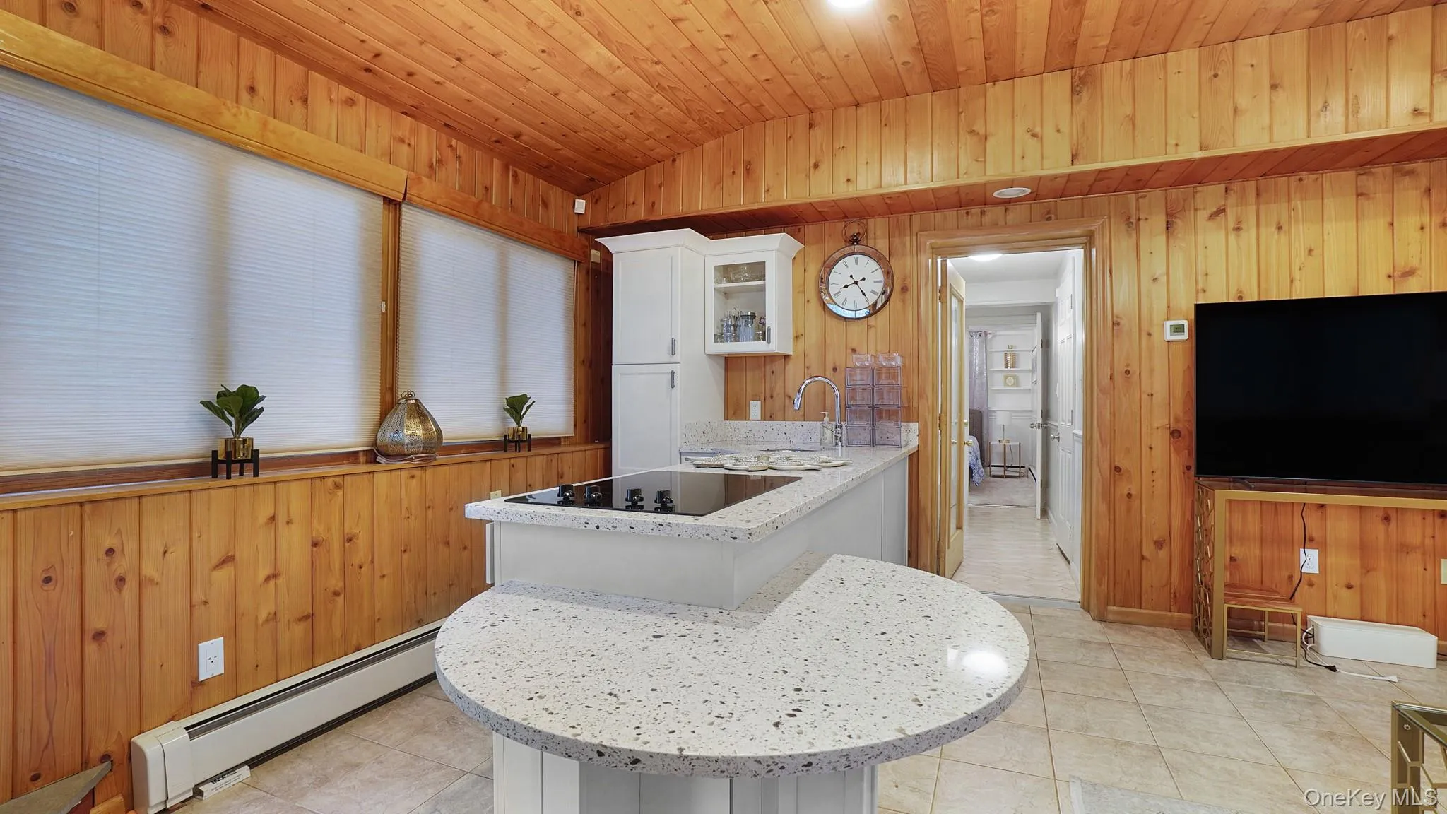 Kitchen featuring wood walls, a baseboard radiator, vaulted ceiling, white cabinets, and a peninsula Kitchen featuring wood walls, a baseboard radiator, vaulted ceiling, white cabinets, and a peninsula