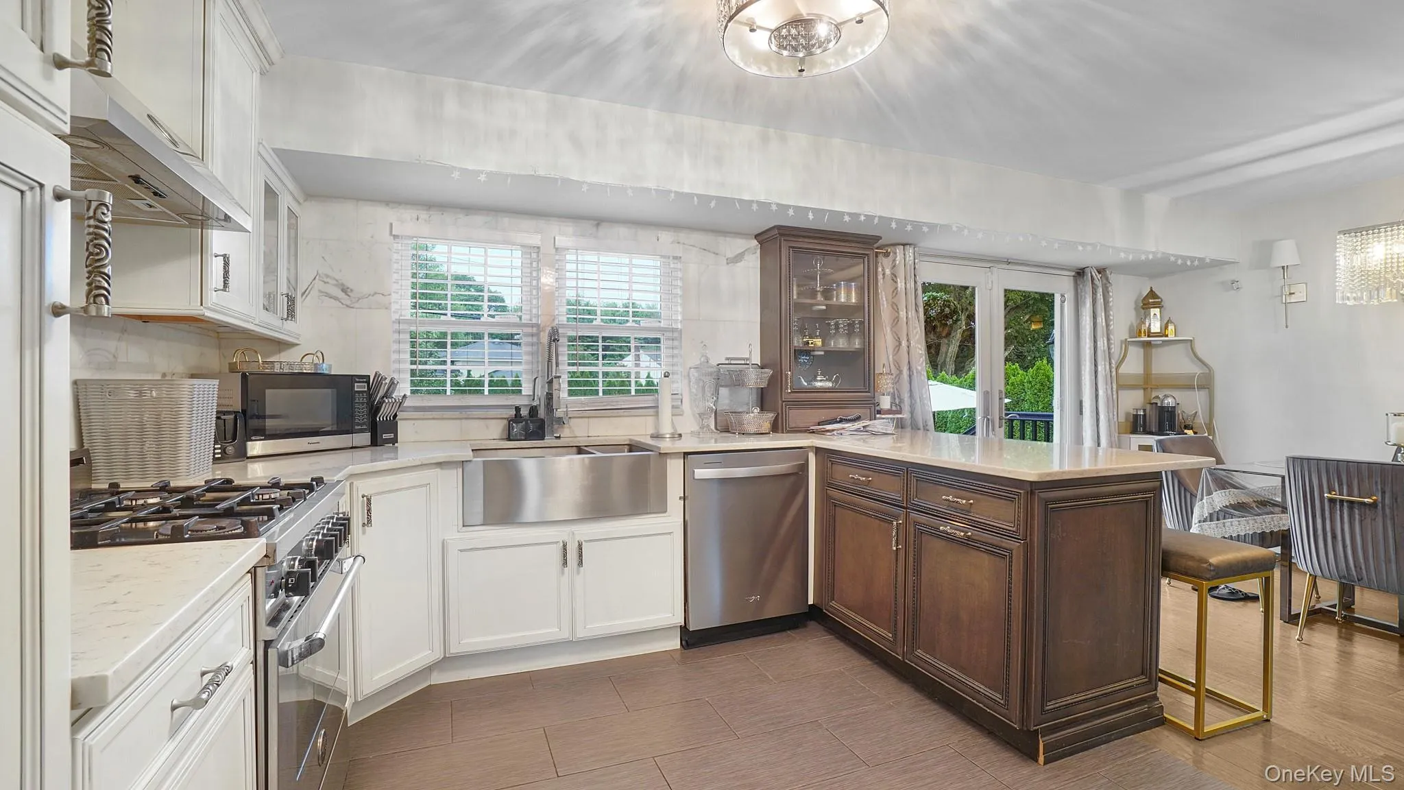 Kitchen with appliances with stainless steel finishes, a peninsula, white cabinets, under cabinet range hood, and glass insert cabinets Kitchen with appliances with stainless steel finishes, a peninsula, white cabinets, under cabinet range hood, and glass insert cabinets