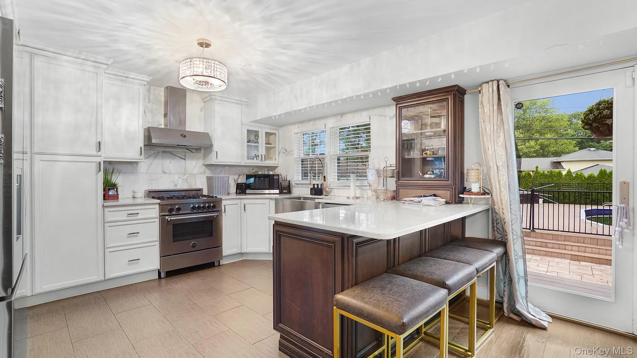 Kitchen featuring stainless steel appliances, a peninsula, light countertops, wall chimney range hood, and glass insert cabinets Kitchen featuring stainless steel appliances, a peninsula, light countertops, wall chimney range hood, and glass insert cabinets