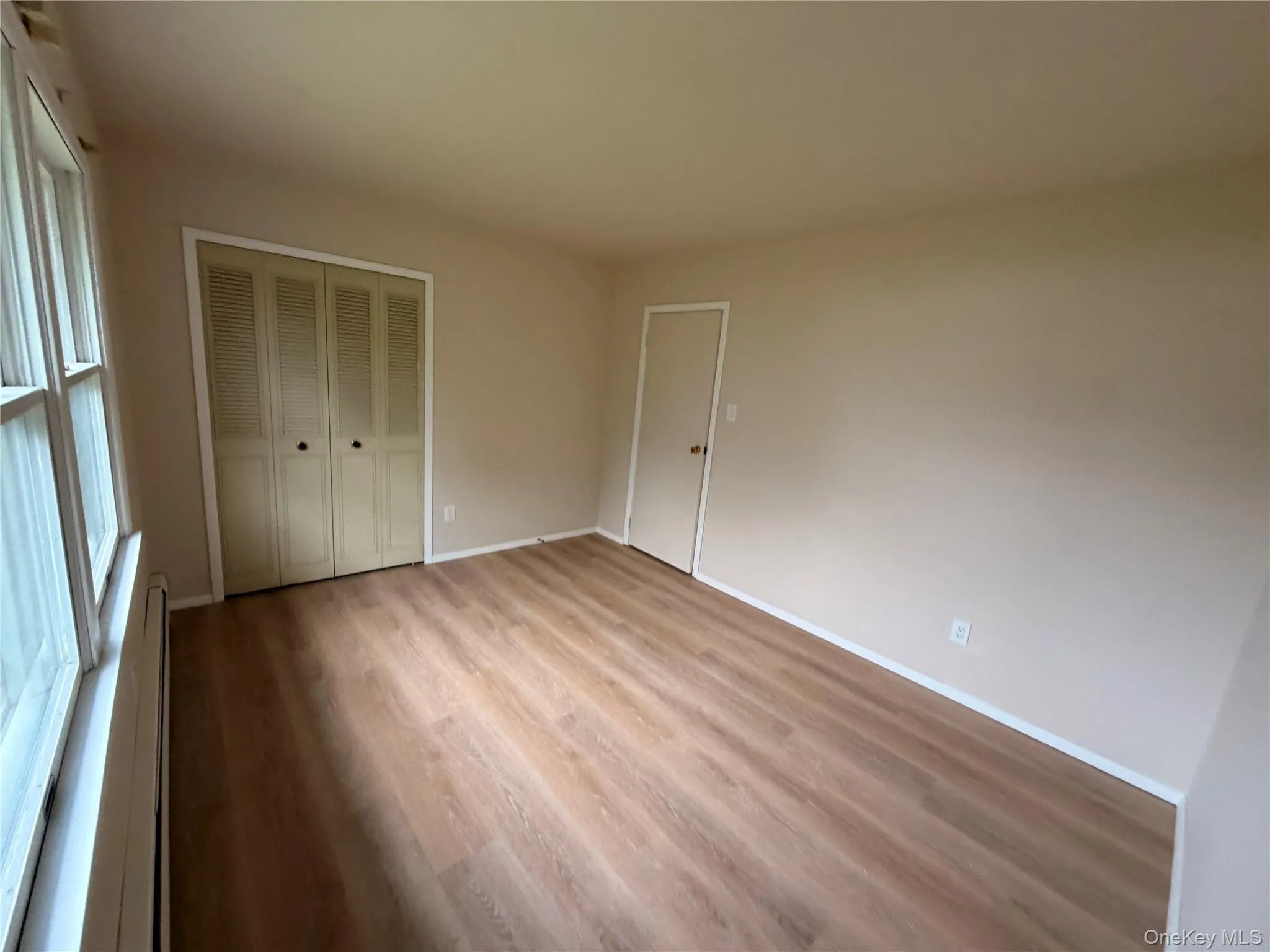 Wood-finish flooring, neutral wall paint, white trim, and a window with white framing Wood-finish flooring, neutral wall paint, white trim, and a window with white framing