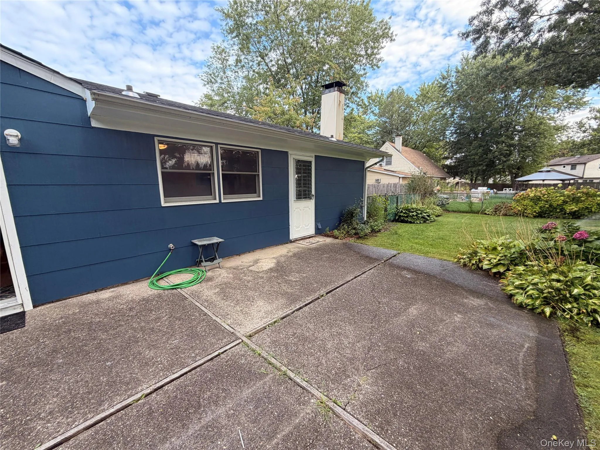 Concrete patio with direct outdoor access, bordered by a vibrant green lawn and established perimeter landscaping Concrete patio with direct outdoor access, bordered by a vibrant green lawn and established perimeter landscaping