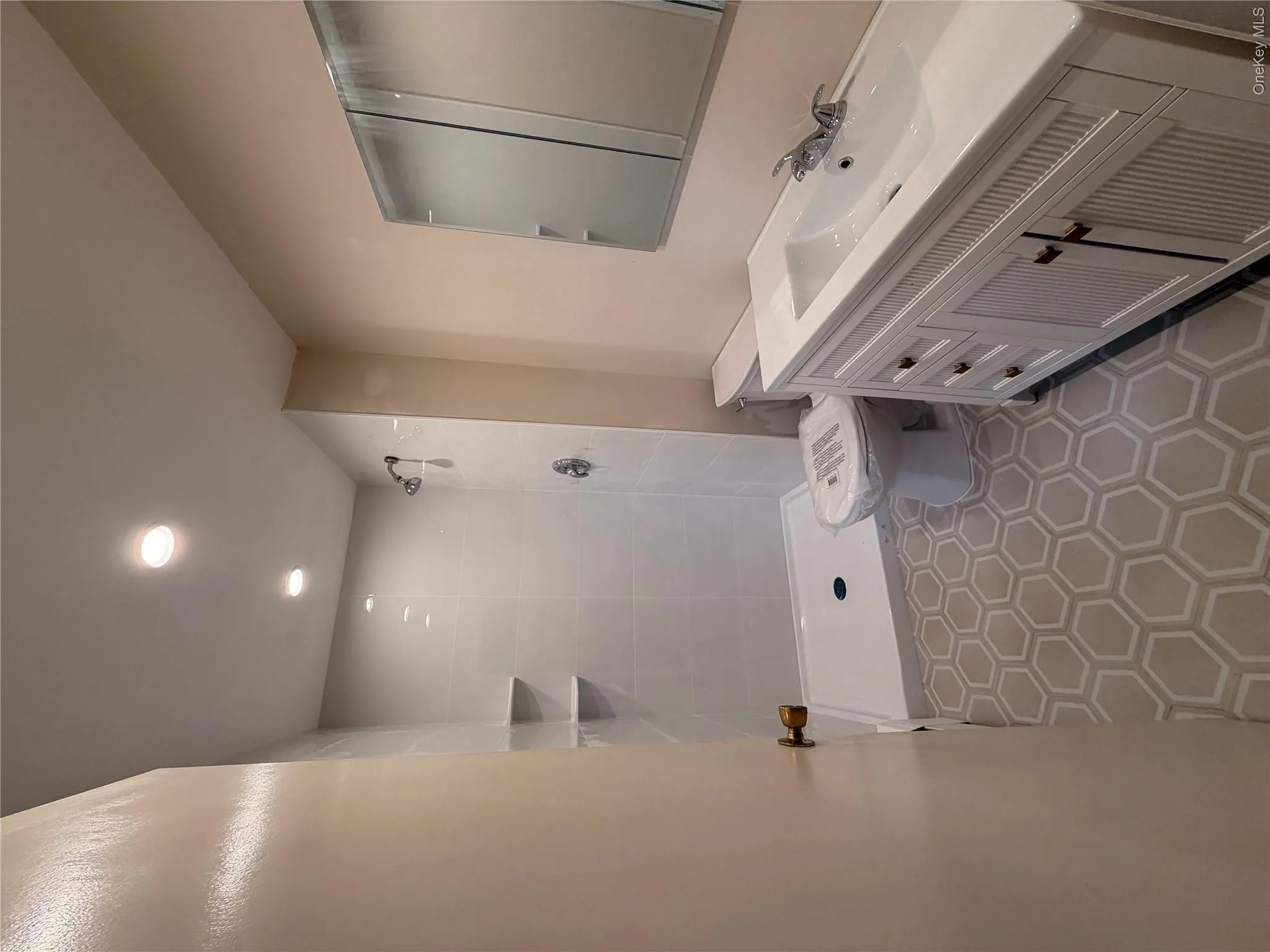 Bathroom featuring hexagon floor tile, white vanity with integrated sink, recessed lighting, white subway tile shower, and built-in shower shelving Bathroom featuring hexagon floor tile, white vanity with integrated sink, recessed lighting, white subway tile shower, and built-in shower shelving