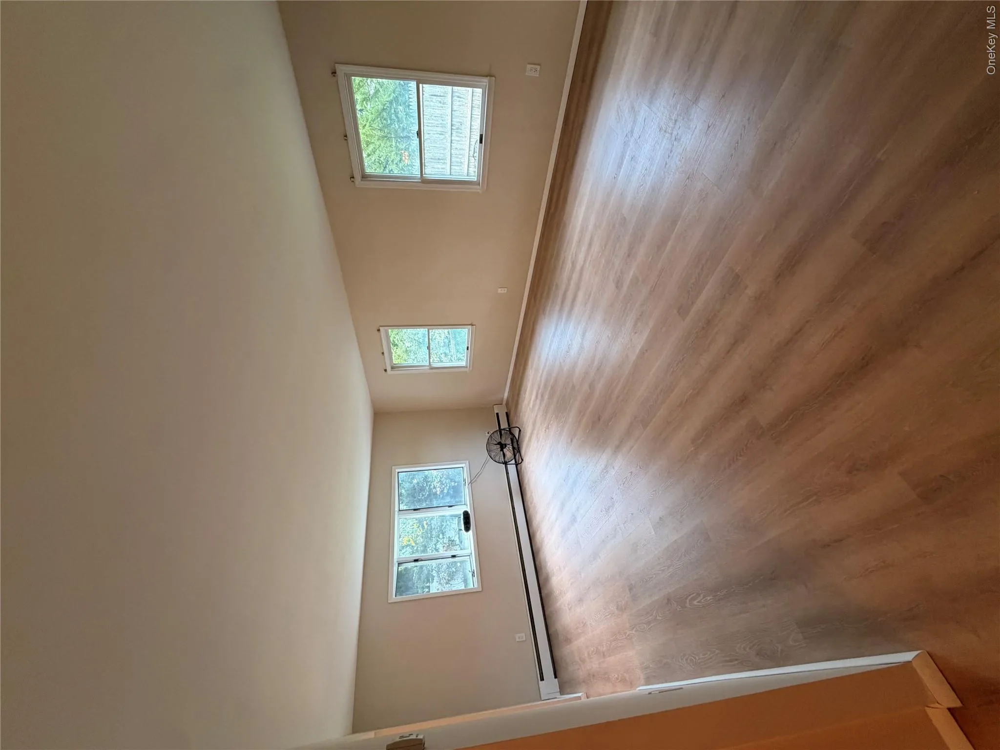Spacious room featuring wood-finish flooring, multiple windows, and a baseboard heating system Spacious room featuring wood-finish flooring, multiple windows, and a baseboard heating system