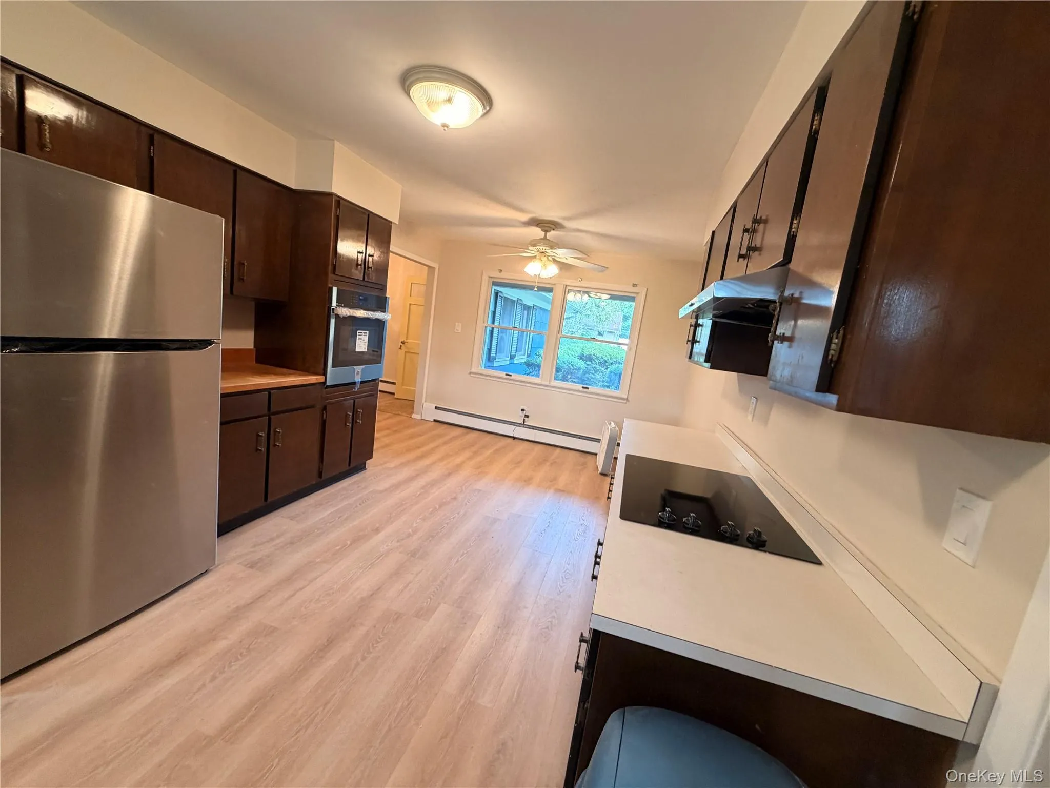 Kitchen featuring dark wood cabinetry, stainless steel appliances, light wood-finish flooring, and white countertops Kitchen featuring dark wood cabinetry, stainless steel appliances, light wood-finish flooring, and white countertops