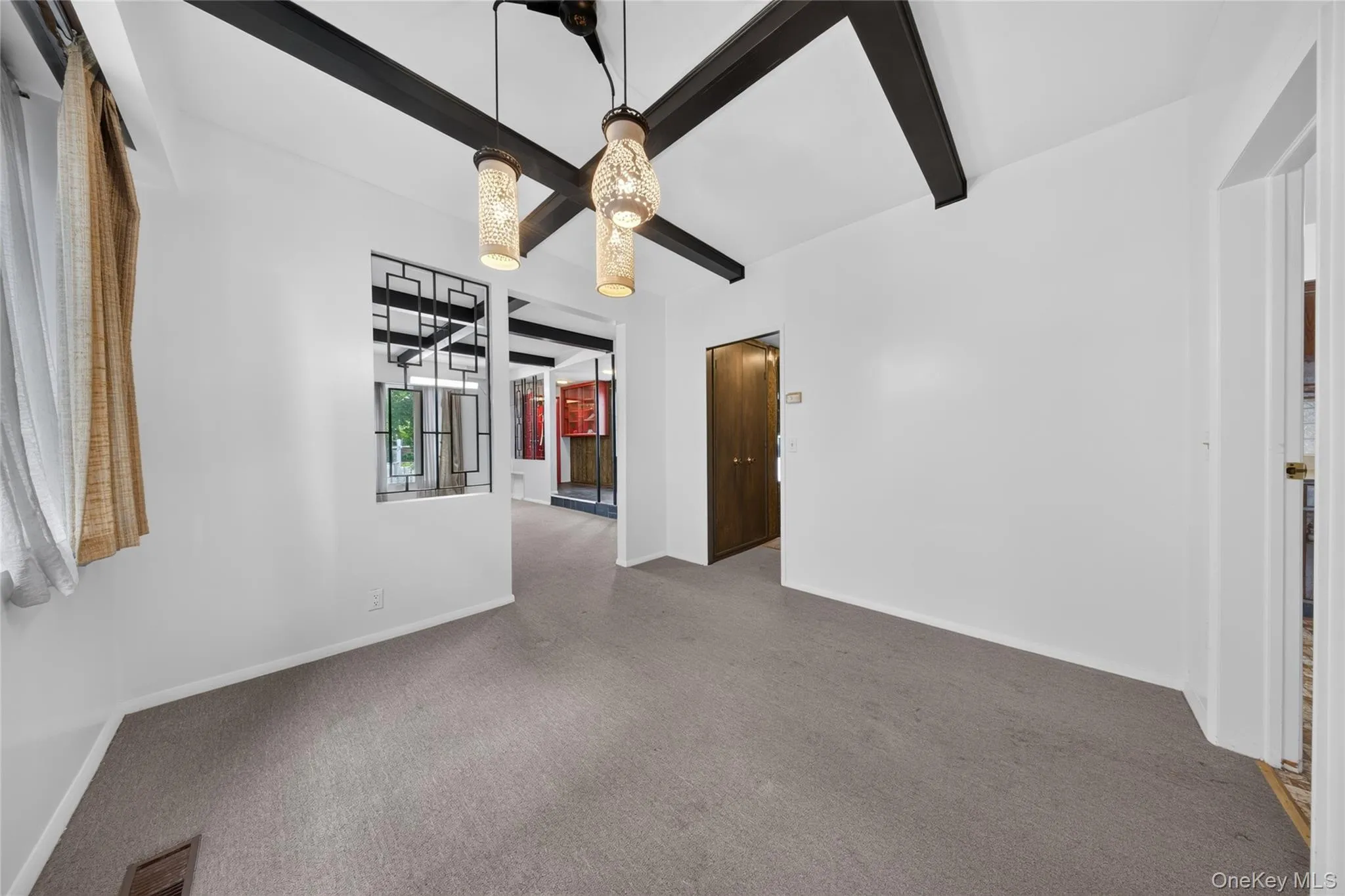 Vaulted ceiling with exposed beams, decorative ceiling light fixtures, wall cut-out with geometric grille, and neutral carpeting Vaulted ceiling with exposed beams, decorative ceiling light fixtures, wall cut-out with geometric grille, and neutral carpeting