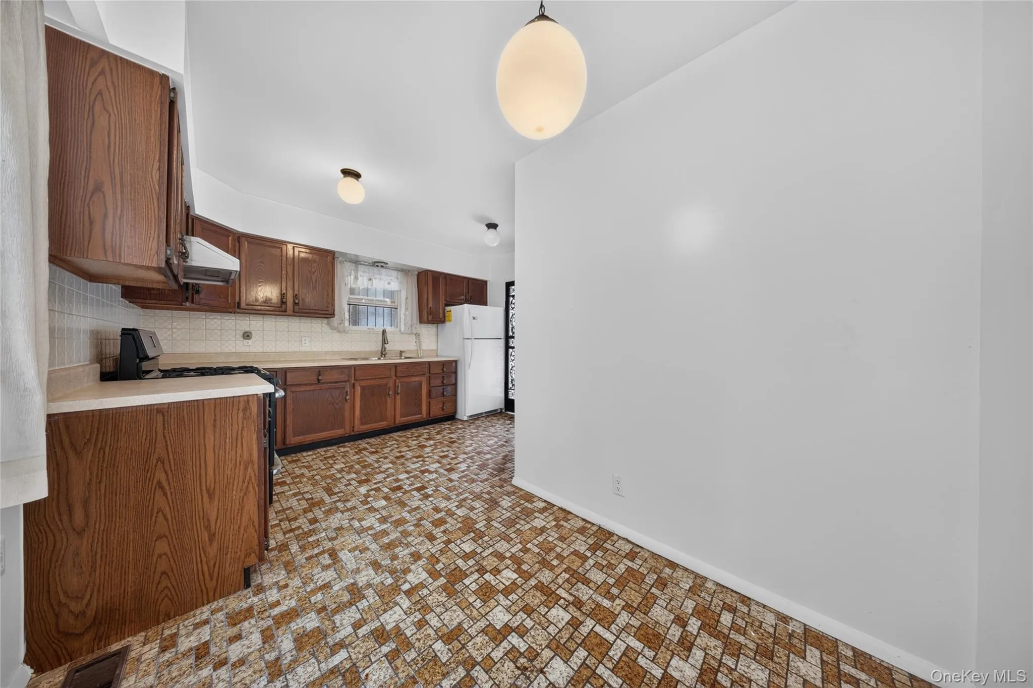 Kitchen featuring wood-finish cabinetry, built-in range hood, white tile backsplash, and patterned flooring Kitchen featuring wood-finish cabinetry, built-in range hood, white tile backsplash, and patterned flooring