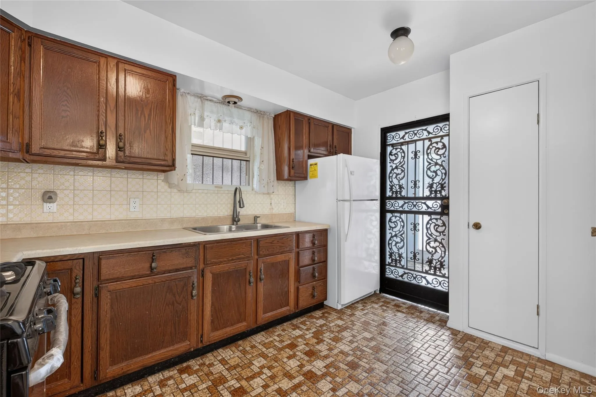 Kitchen featuring wood cabinetry, a double basin sink, light-toned countertops, and a patterned tile backsplash Kitchen featuring wood cabinetry, a double basin sink, light-toned countertops, and a patterned tile backsplash