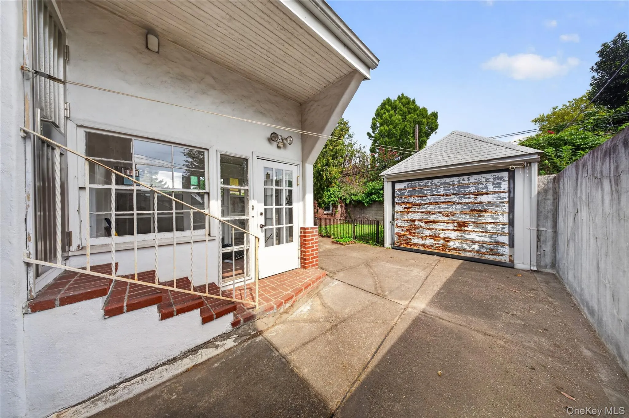 Attached garage with pitched roof, concrete driveway, and brick entry steps with metal railing Attached garage with pitched roof, concrete driveway, and brick entry steps with metal railing
