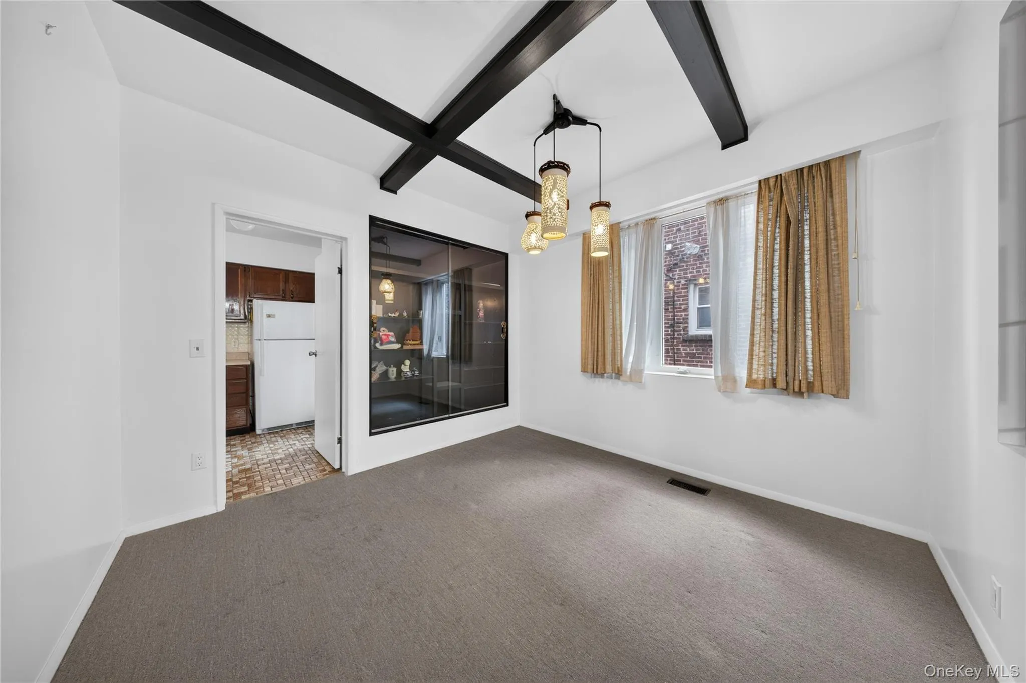 Exposed ceiling beams, suspended light fixture, large window, built-in display case, and wall-to-wall carpeting Exposed ceiling beams, suspended light fixture, large window, built-in display case, and wall-to-wall carpeting