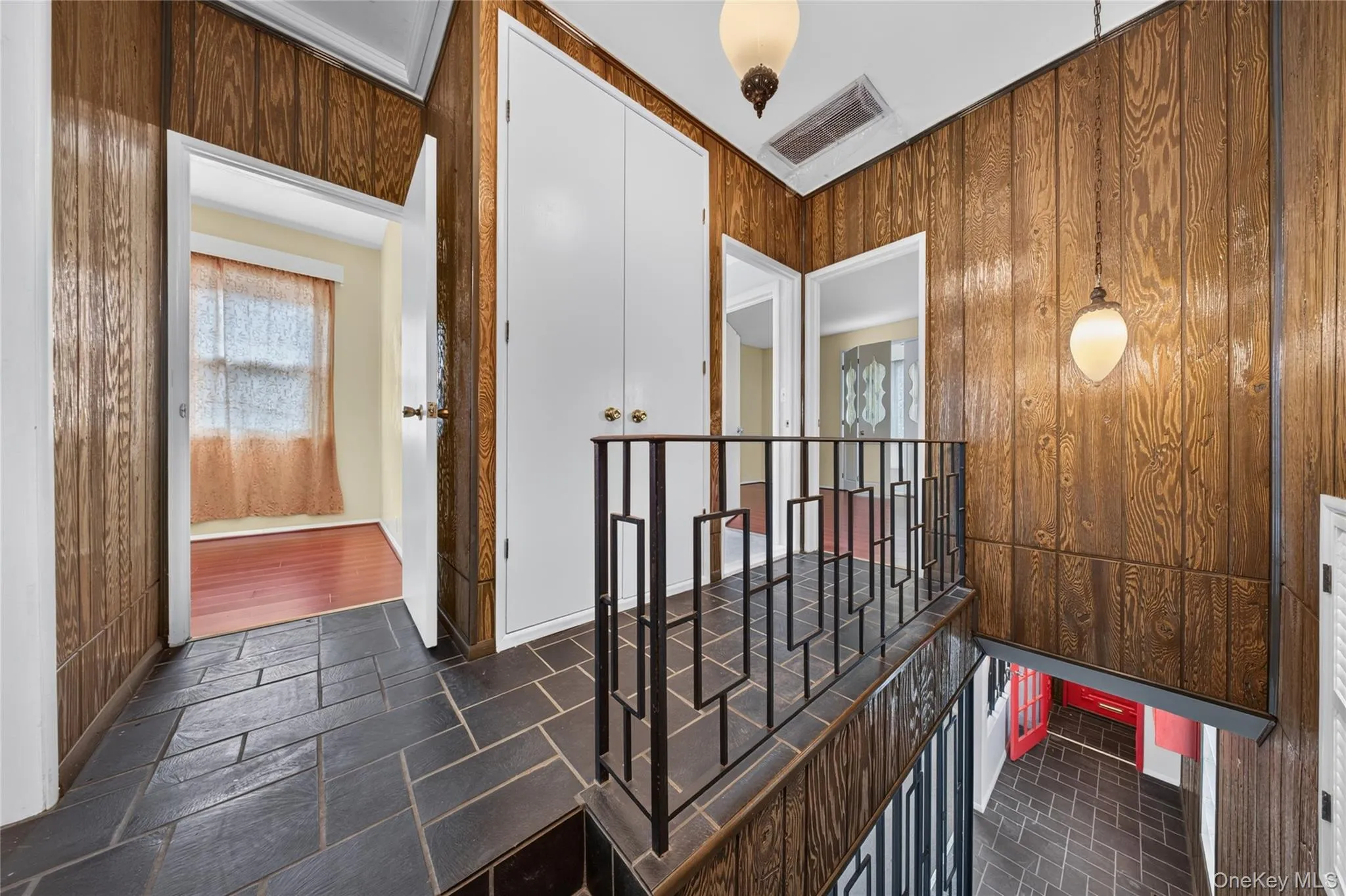 Dark slate tile flooring, wood-paneled walls, white paneled doors, and a decorative metal railing Dark slate tile flooring, wood-paneled walls, white paneled doors, and a decorative metal railing