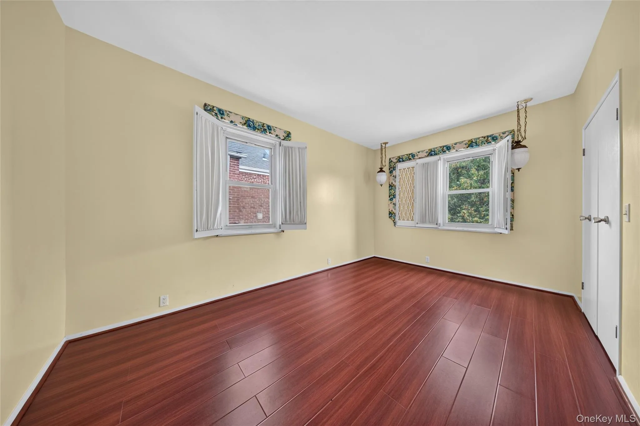 Wood-finish flooring, two windows with shutters, and a white door with silver hardware Wood-finish flooring, two windows with shutters, and a white door with silver hardware