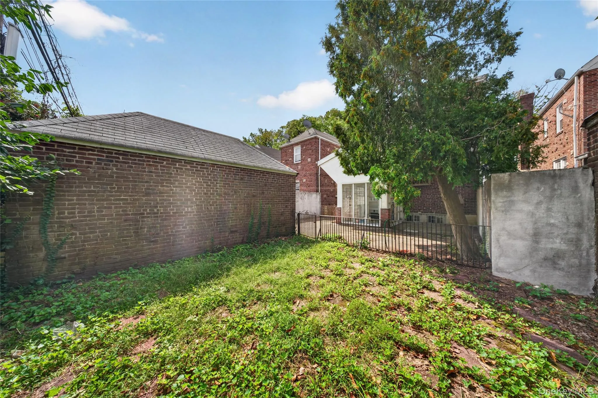 Expansive rear yard featuring mature trees, a brick-clad detached structure, and a fenced patio area Expansive rear yard featuring mature trees, a brick-clad detached structure, and a fenced patio area