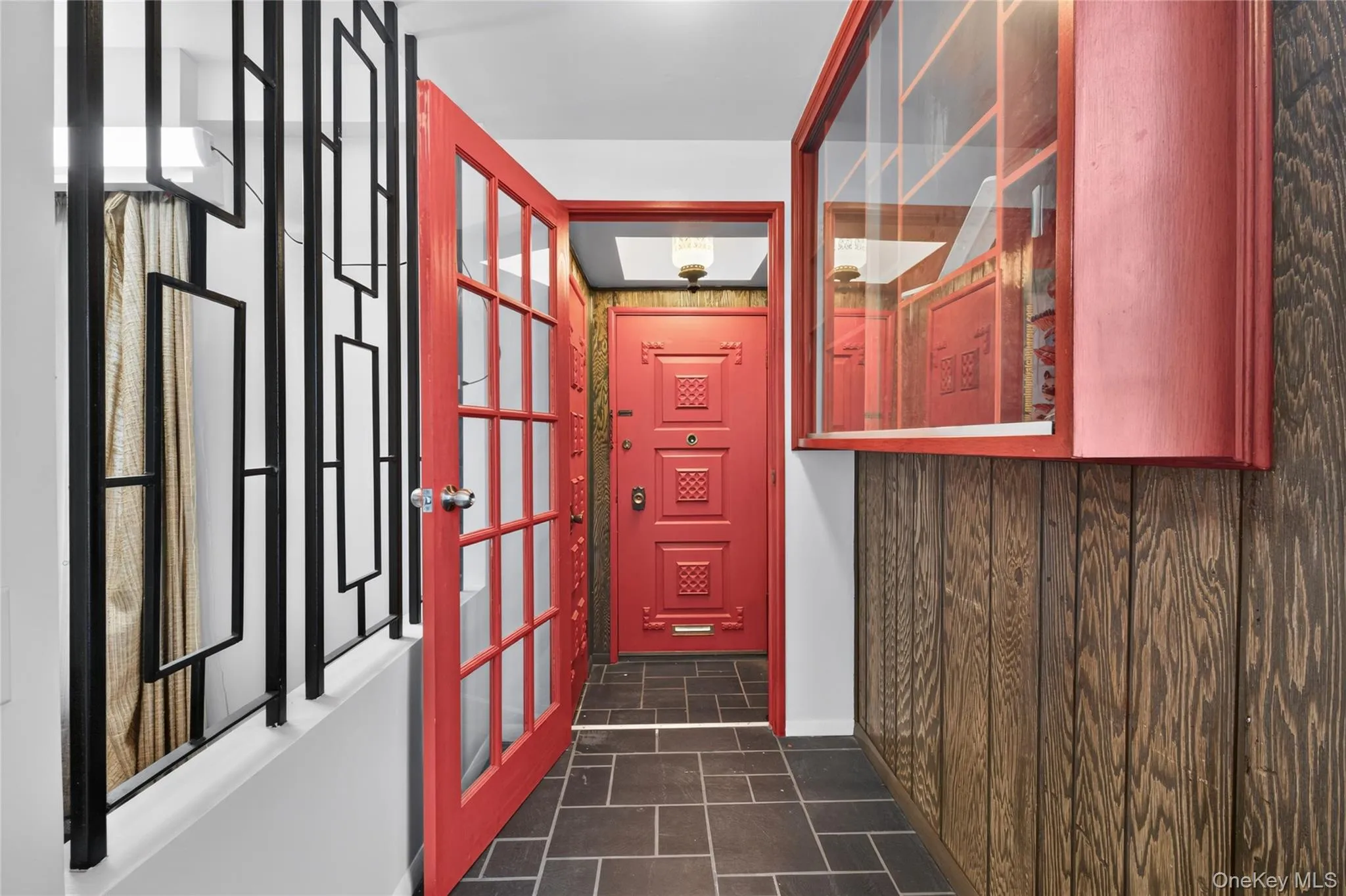 Entryway featuring a decorative metal railing, a glass-paneled door, stone tile flooring, and wood-paneled walls with a built-in display cabinet Entryway featuring a decorative metal railing, a glass-paneled door, stone tile flooring, and wood-paneled walls with a built-in display cabinet