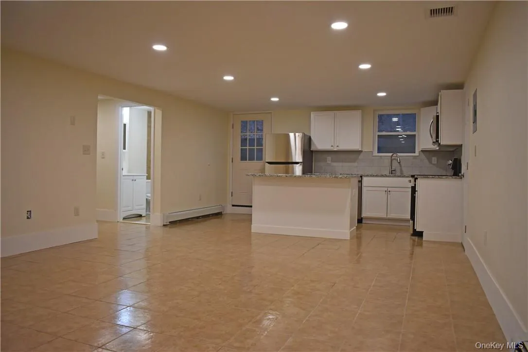Open-concept living space with tile flooring, recessed lighting, and a kitchen featuring white cabinetry and stainless steel appliances Open-concept living space with tile flooring, recessed lighting, and a kitchen featuring white cabinetry and stainless steel appliances