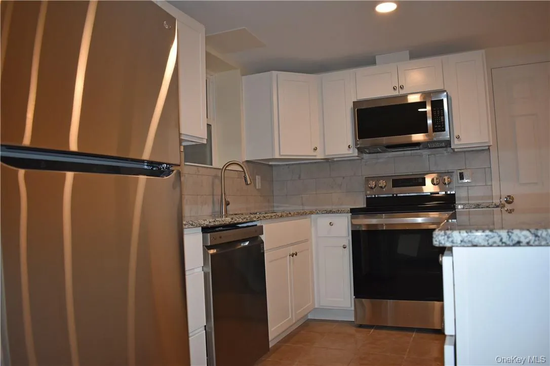 Kitchen featuring white cabinetry, granite countertops, stainless steel appliances, a tile backsplash, and tile flooring Kitchen featuring white cabinetry, granite countertops, stainless steel appliances, a tile backsplash, and tile flooring