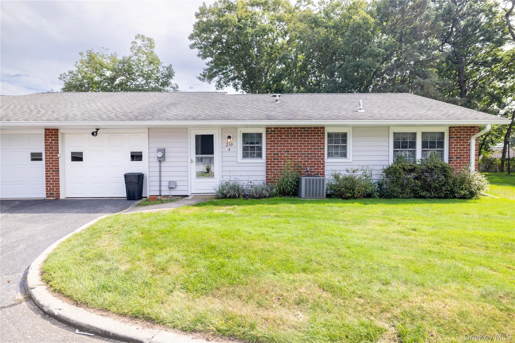 Rear exterior featuring brick and siding facade, an attached garage, a paved driveway, and a manicured lawn Rear exterior featuring brick and siding facade, an attached garage, a paved driveway, and a manicured lawn