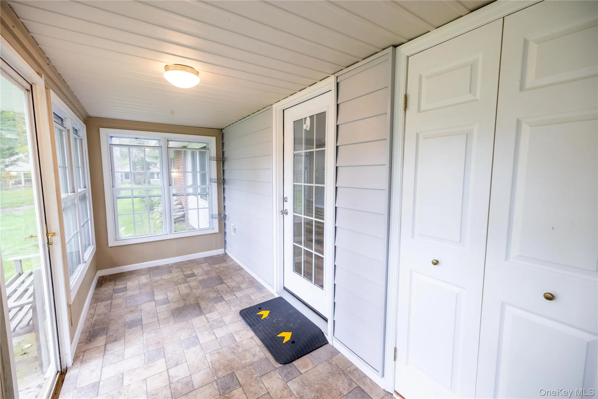 Enclosed porch featuring multiple windows, a paneled ceiling, patterned floor tiles, and a white interior door Enclosed porch featuring multiple windows, a paneled ceiling, patterned floor tiles, and a white interior door