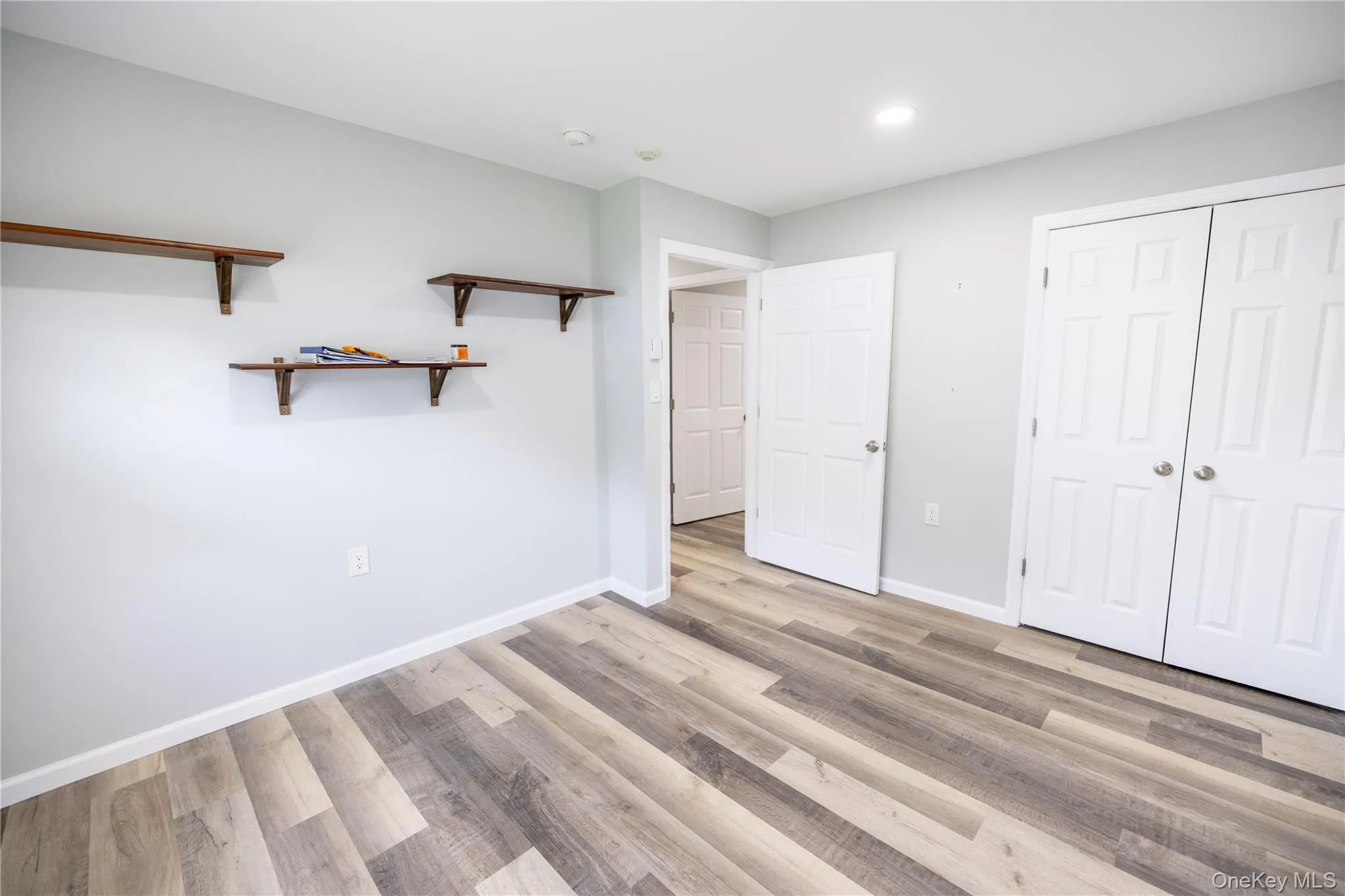 Wood-finish flooring with varying plank widths, light gray wall paint, white trim, recessed lighting, and built-in shelving units Wood-finish flooring with varying plank widths, light gray wall paint, white trim, recessed lighting, and built-in shelving units