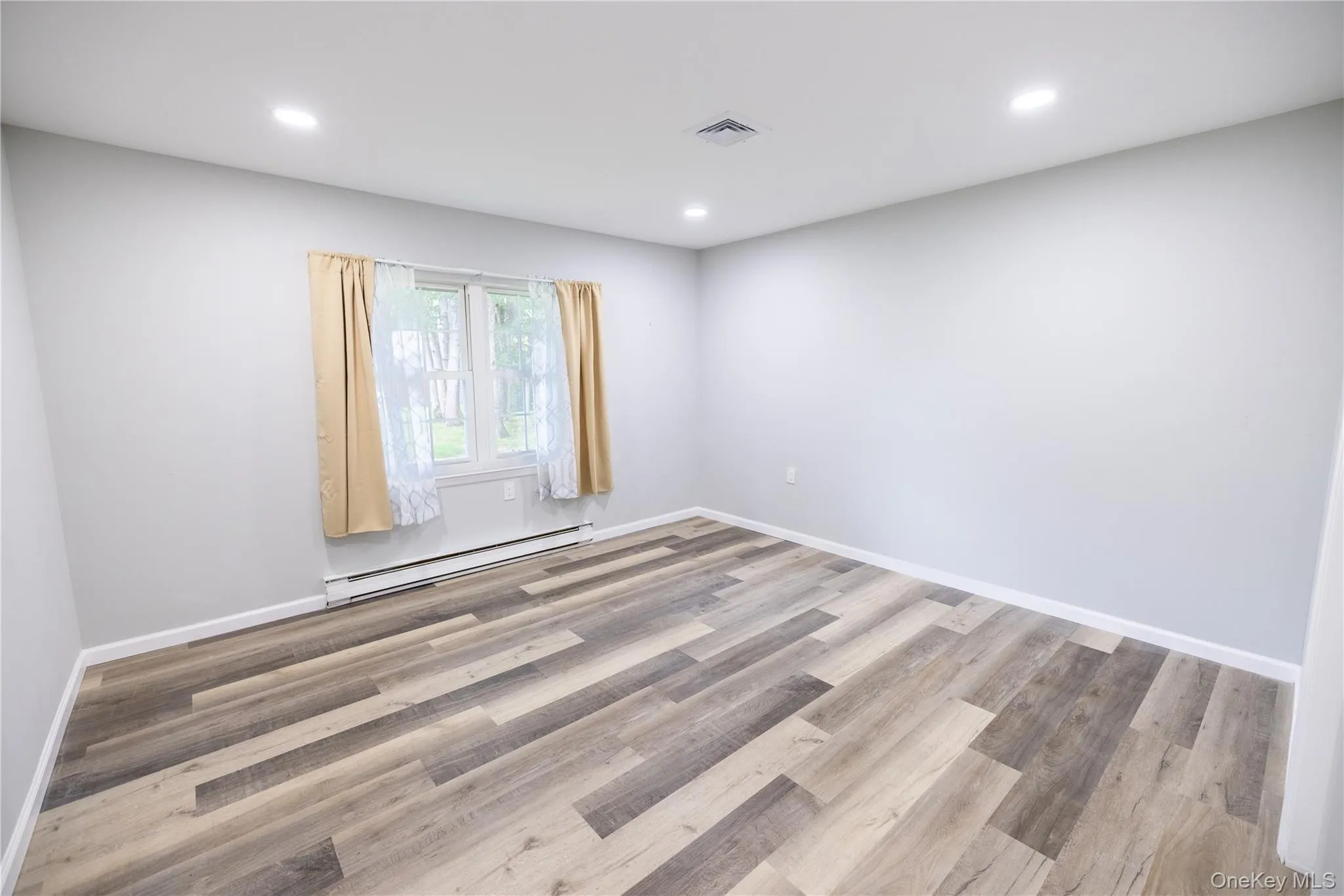 Recessed lighting, light gray walls, wood-finish flooring, and baseboard heating Recessed lighting, light gray walls, wood-finish flooring, and baseboard heating