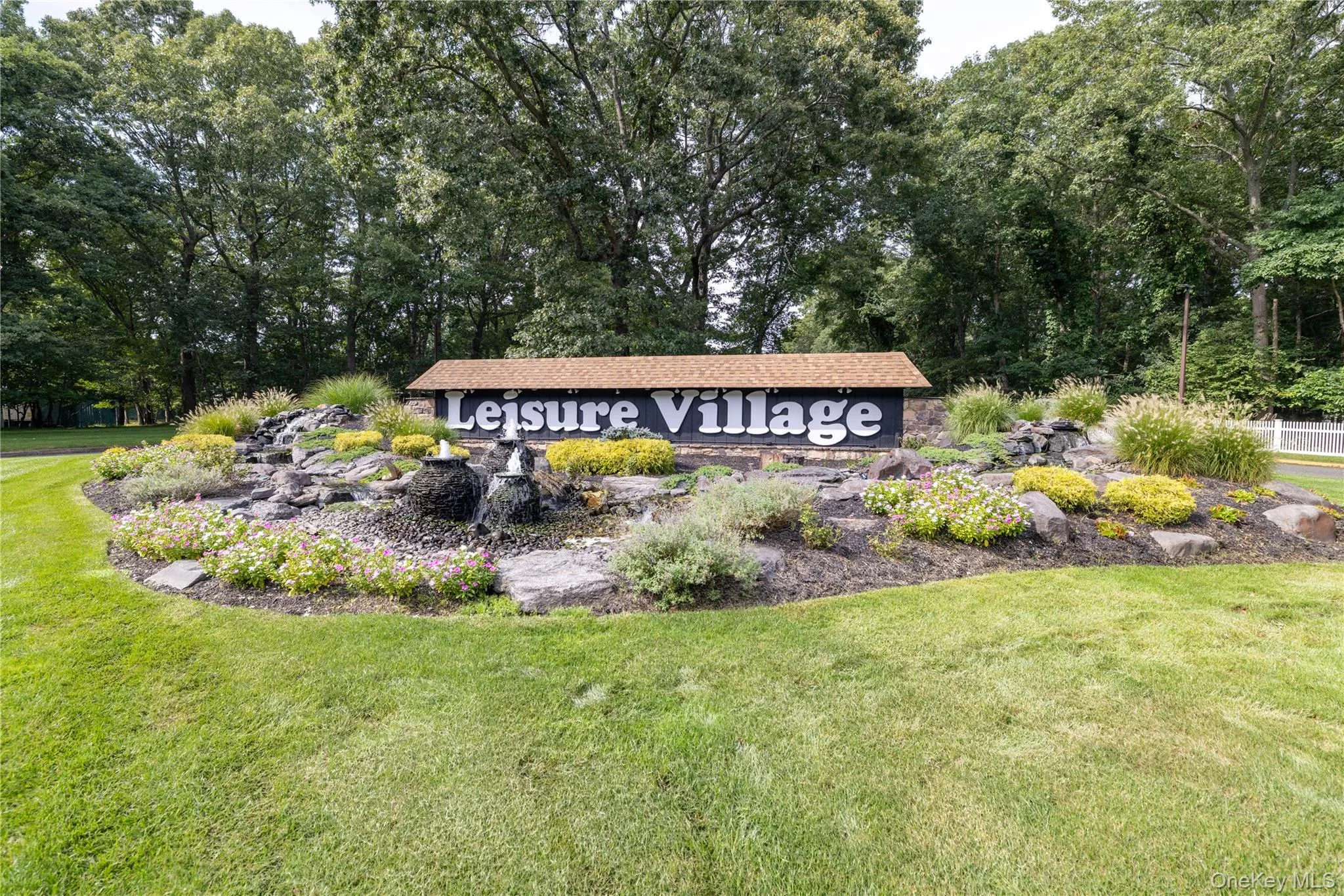Community signage with prominent lettering, a stone water feature, layered landscaping, and surrounding mature trees Community signage with prominent lettering, a stone water feature, layered landscaping, and surrounding mature trees